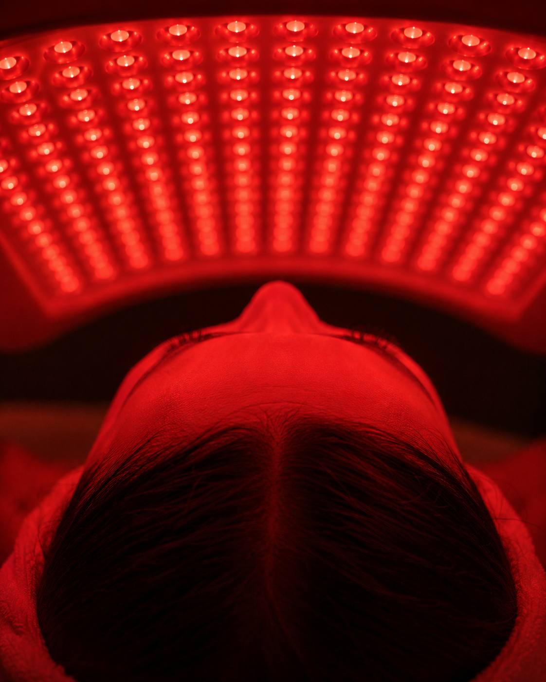Red light therapy panel illuminating hair and scalp, representing gentle LED skin therapy for recovery without downtime.