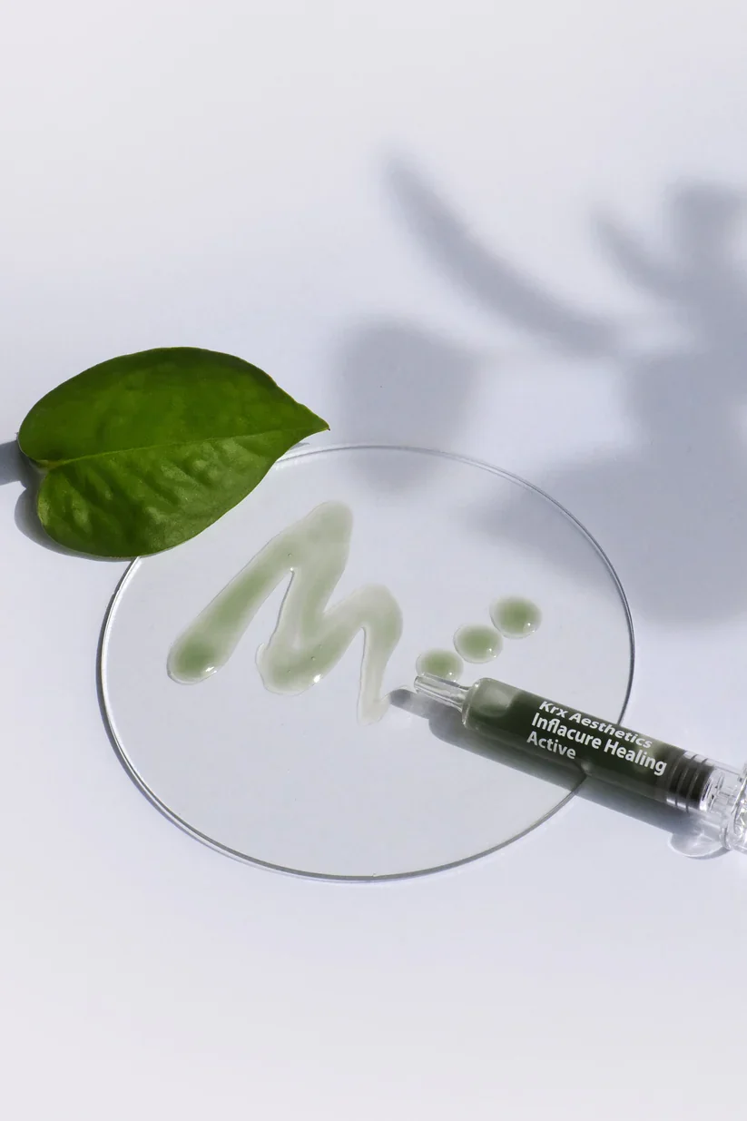 A glass petri dish with a green leaf, a syringe labeled 'Active Healing,' and some clear liquid and droplets on a white background, with shadows cast on the surface.