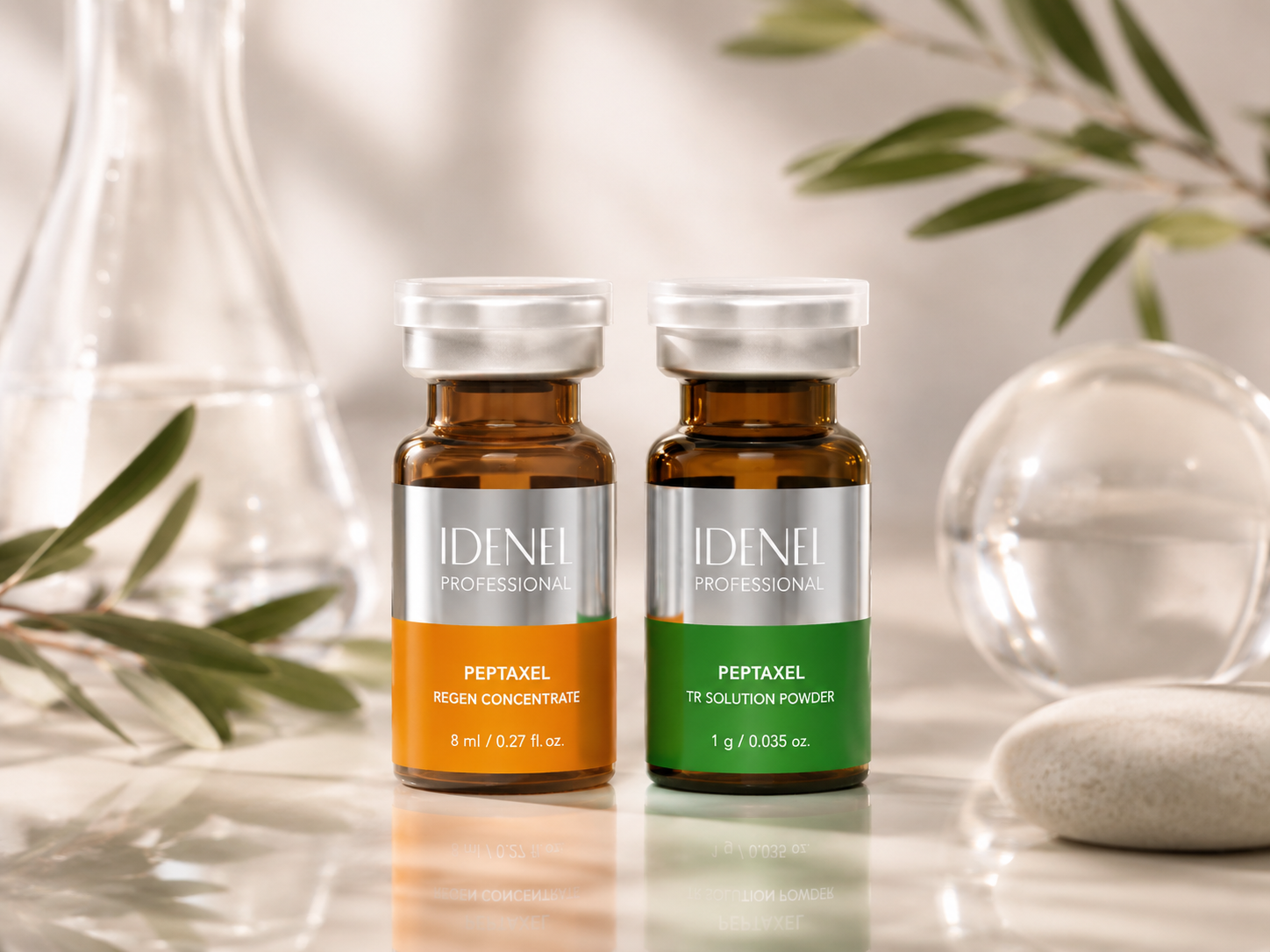 Two small bottles labeled 'IDENEL PROFESSIONAL' with orange and green labels, set on a marble surface with glassware and green leaves in the background.