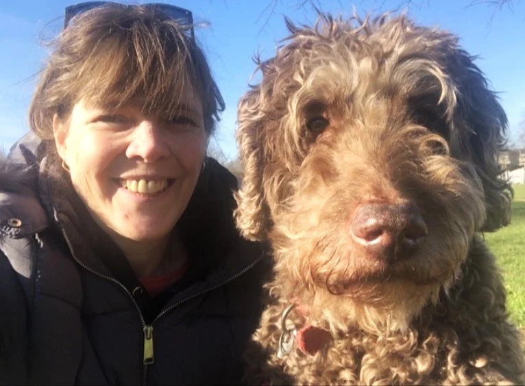 Women next to brown Labradoodle dog in the outdoors 