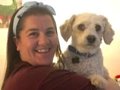 A happy lady holding a white Cavachon dog