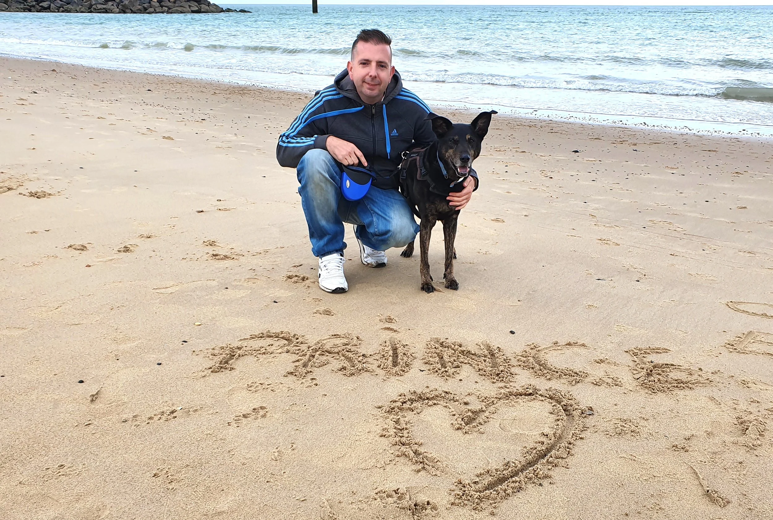man and dog on beach front, "prince" written in the sand