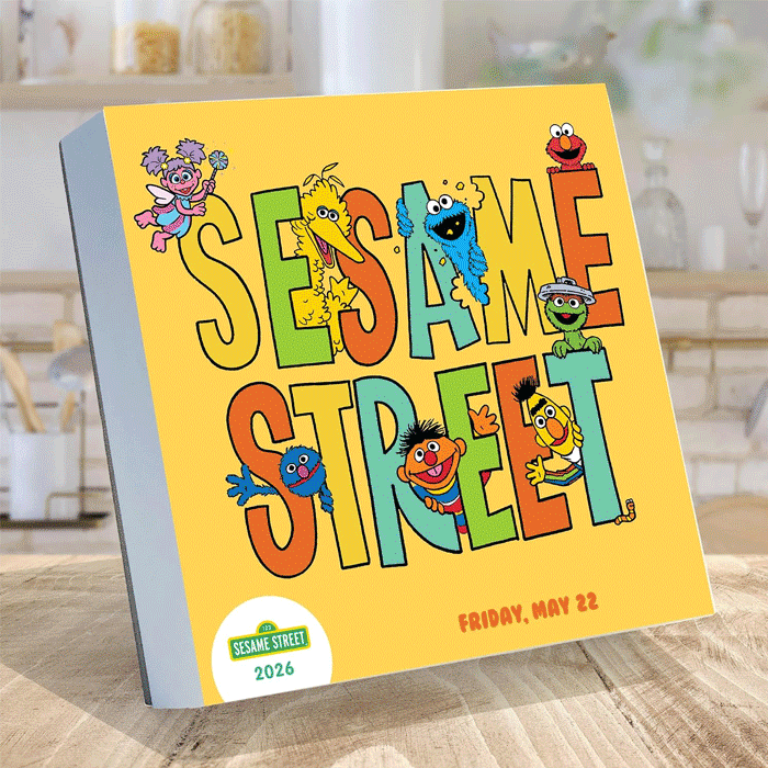 Colorful children's book cover titled 'Sesame Street Some Stret' with Sesame Street characters and the date 'Friday, May 22.' The cover features a yellow background and a sticker with the Sesame Street logo and the year 2026.