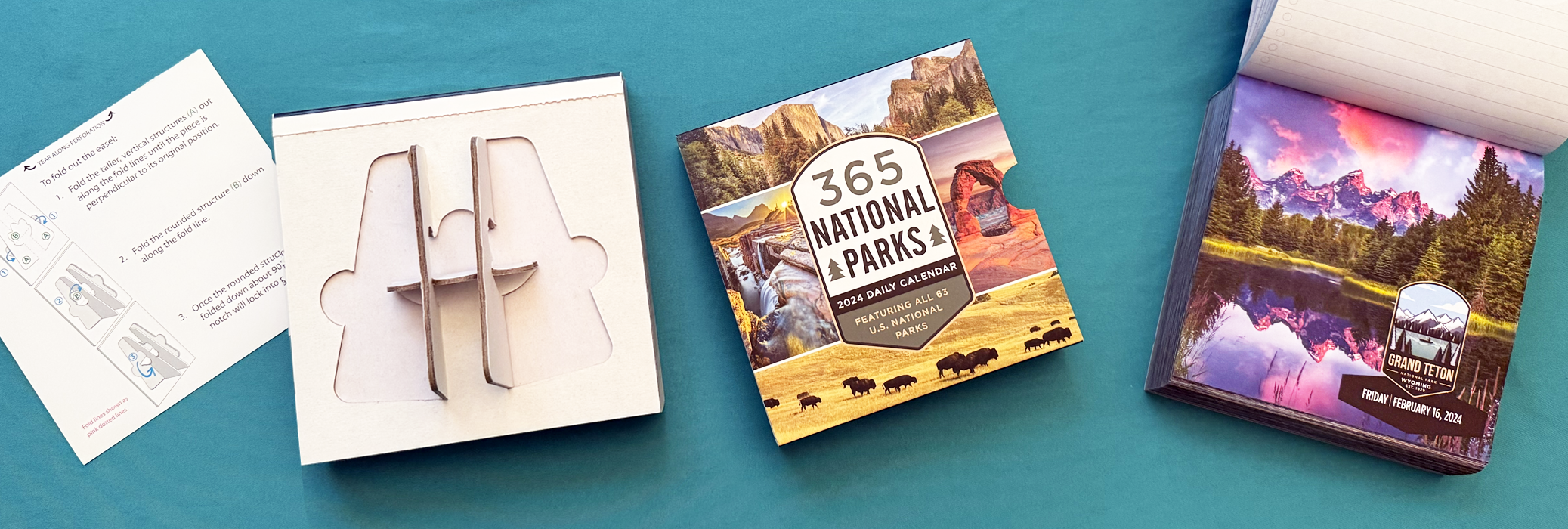 A desk with a 2024 daily calendar of U.S. national parks, a small puzzle of a mountain elk, a stack of landscape photographs, and instruction sheets for assembling the puzzle.
