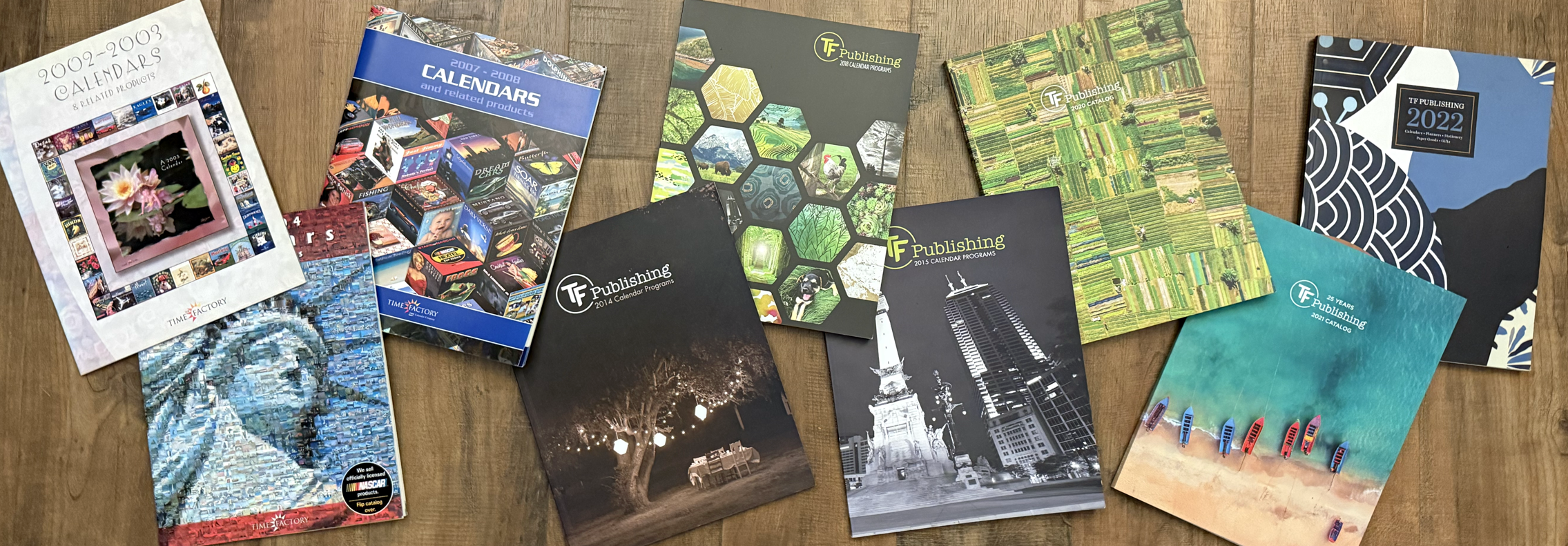 A collection of various calendars and printed booklets spread out on a wooden surface, featuring images of flowers, cityscapes, nature, and abstract patterns.