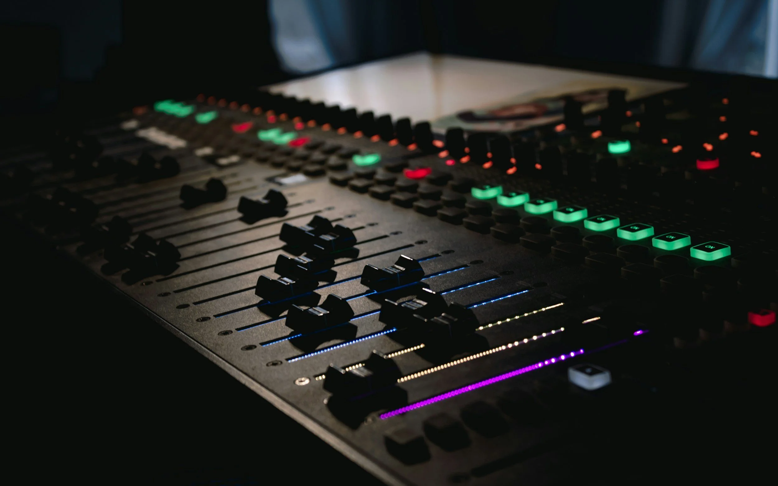 An audio mixing console with various illuminated controls, buttons, and sliders.