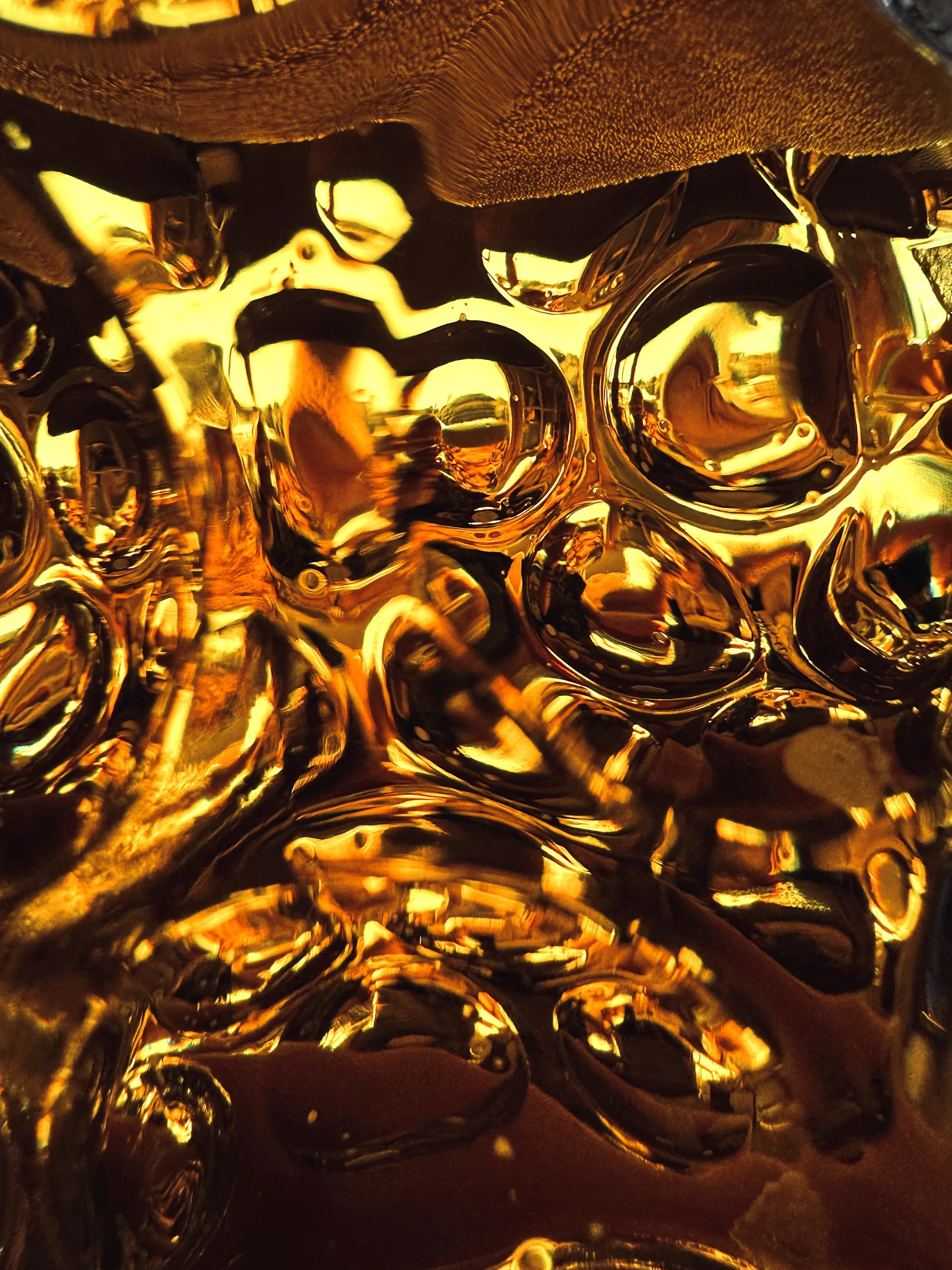 Ein metallic-glänzendes, goldfarbenes, reflektierendes Objekt mit geschwungenen Mustern und Oberflächen, die Licht reflektieren, vermutlich eine dekorative oder künstlerische Skulptur.