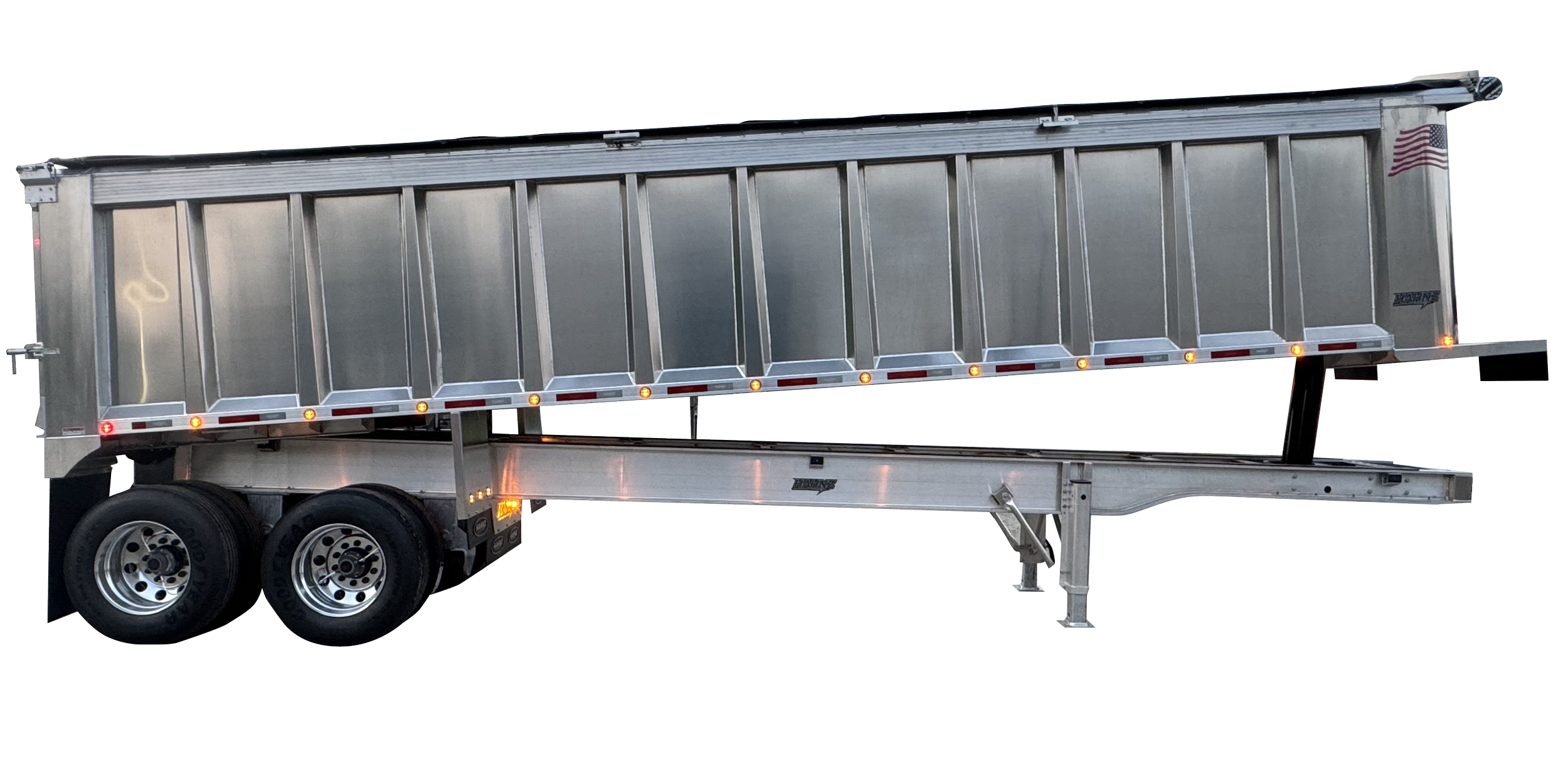 Silver flatbed trailer with dual axles and black tires, equipped with a raised front end, set against a black background.