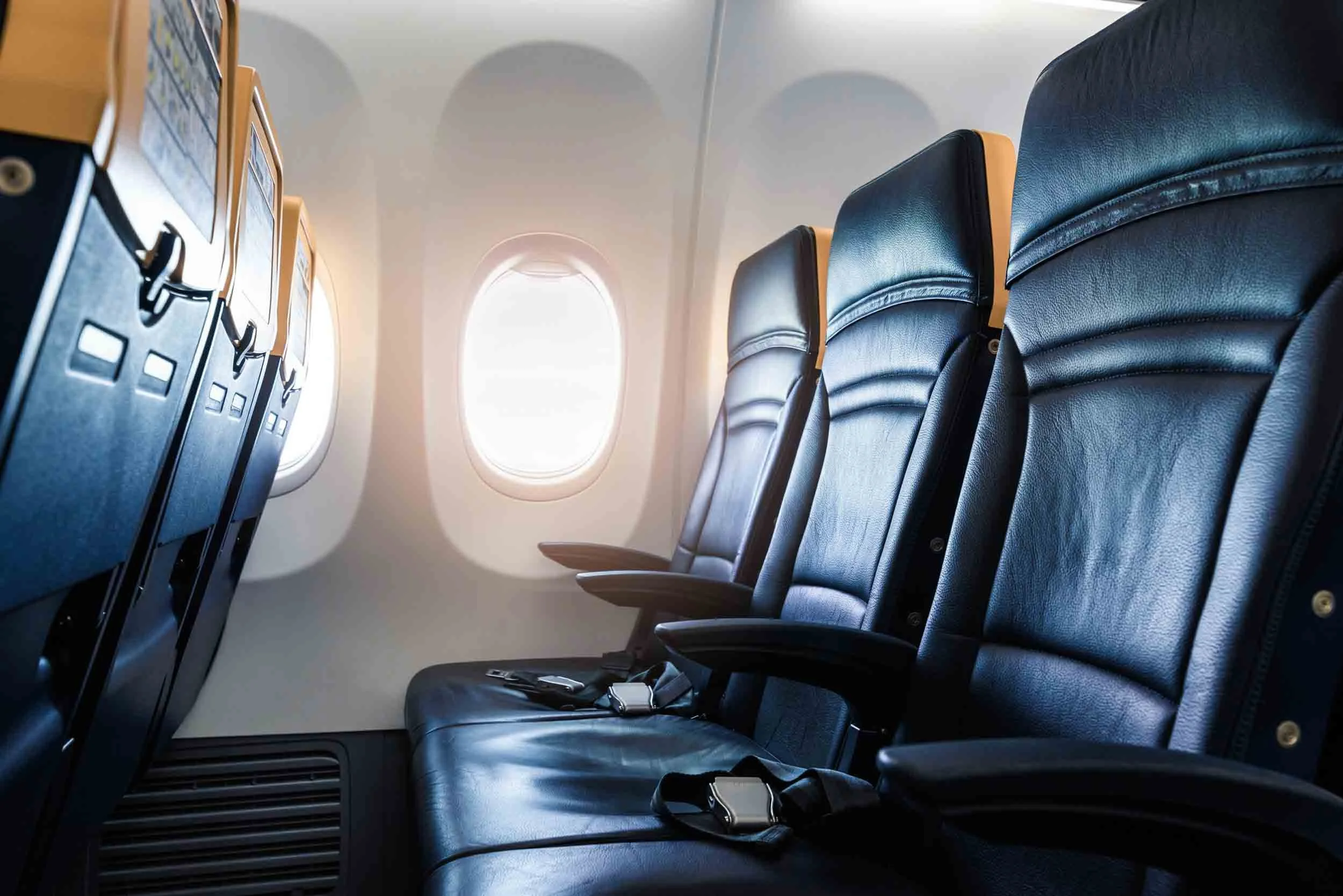 Interior of an airplane cabin showing multiple black leather seats with yellow headrests, a window, and overhead compartments.