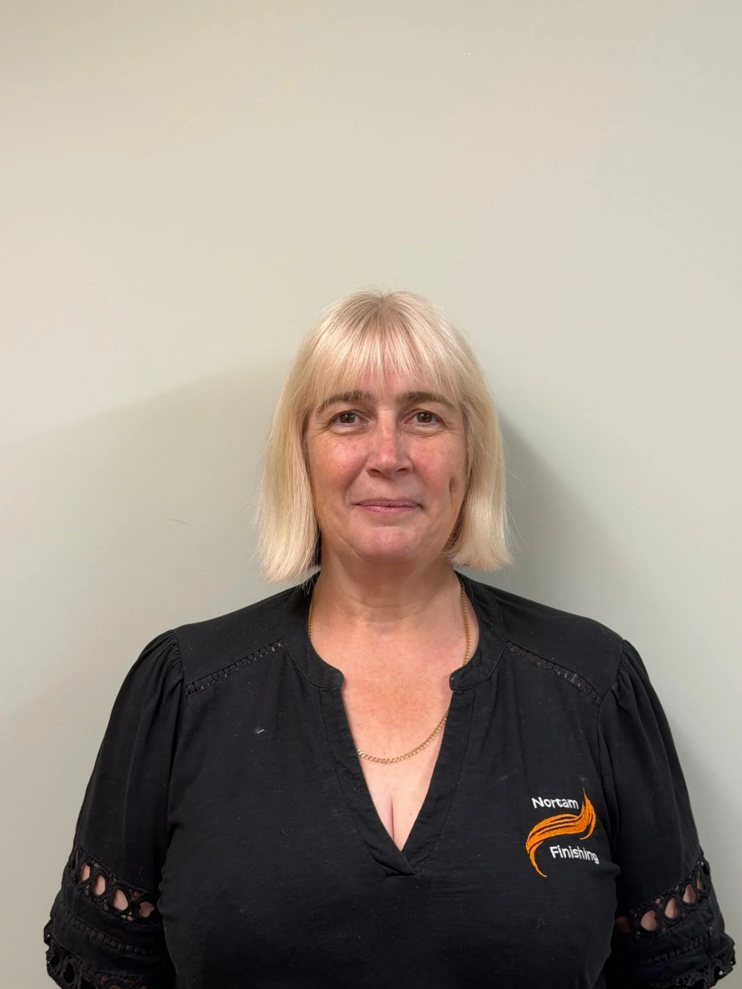 A woman with blonde hair wearing a black shirt with orange and white logo that says 'Northam Finishing'.