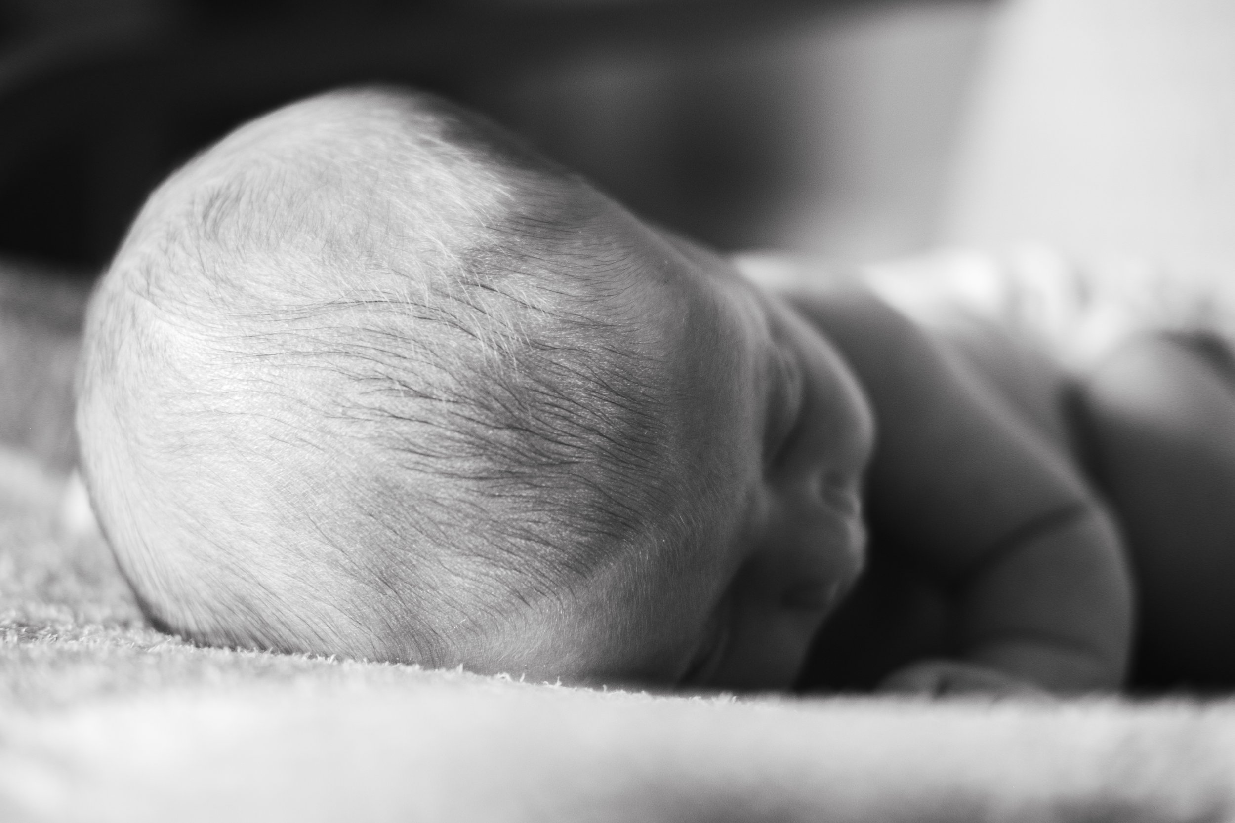 Close-up black and white photo of a sleeping baby, showing the top of the head with soft, fine hair, resting on a surface.