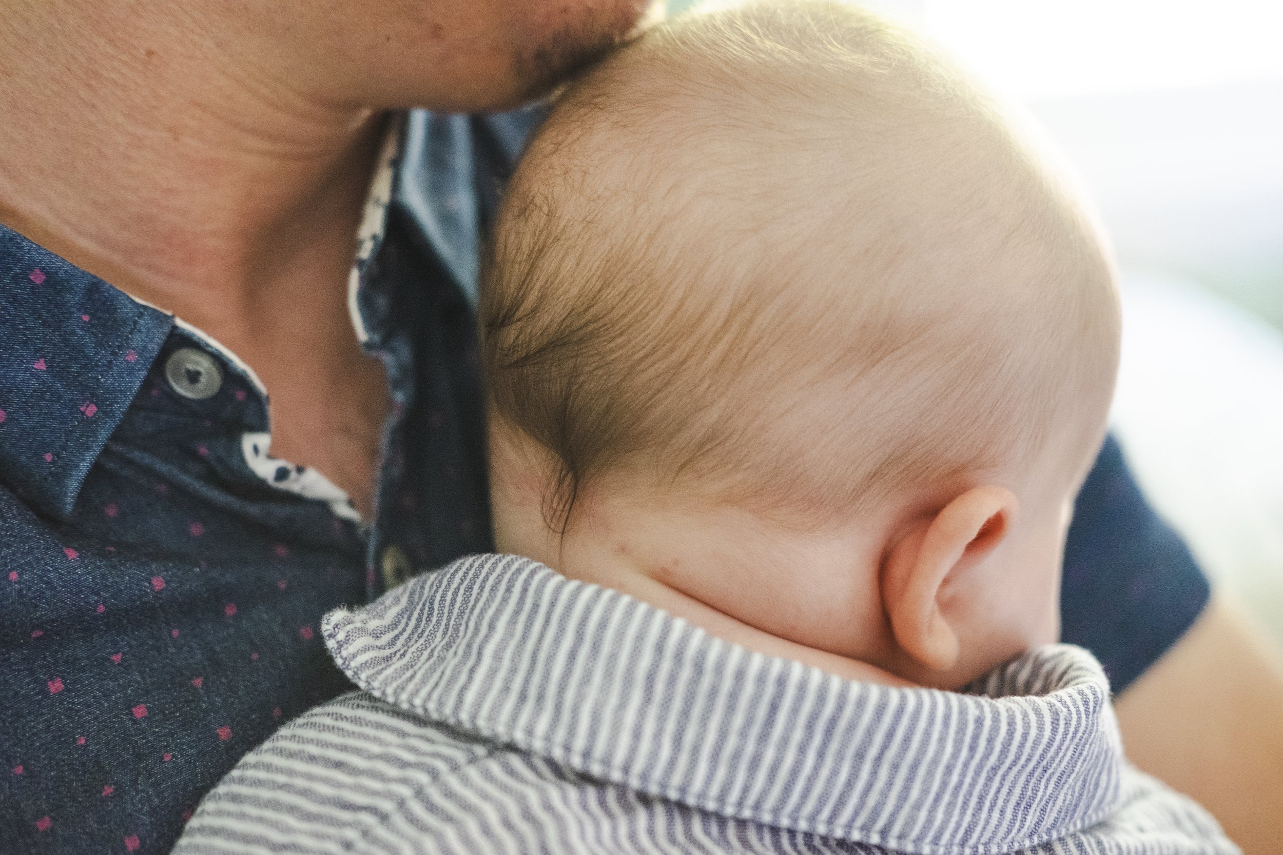 Close-up of a parent holding a sleeping baby, focusing on the parent's chin and baby's head, with soft natural lighting.