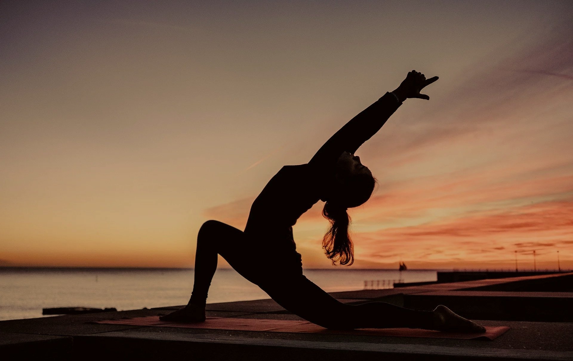 Silhouette d'une femme faisant du yoga au coucher du soleil près de la mer.