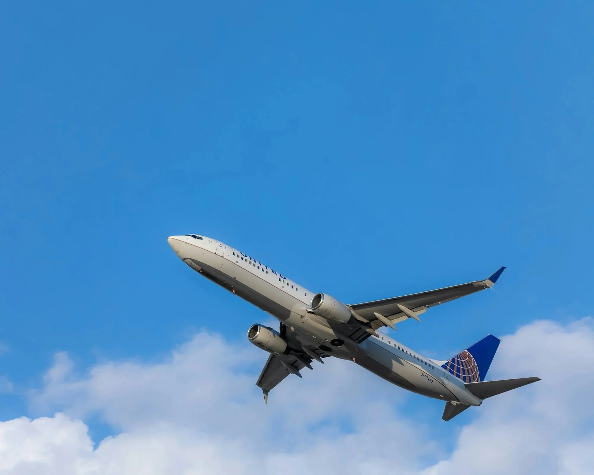 A commercial airplane flying through a blue sky with some clouds.