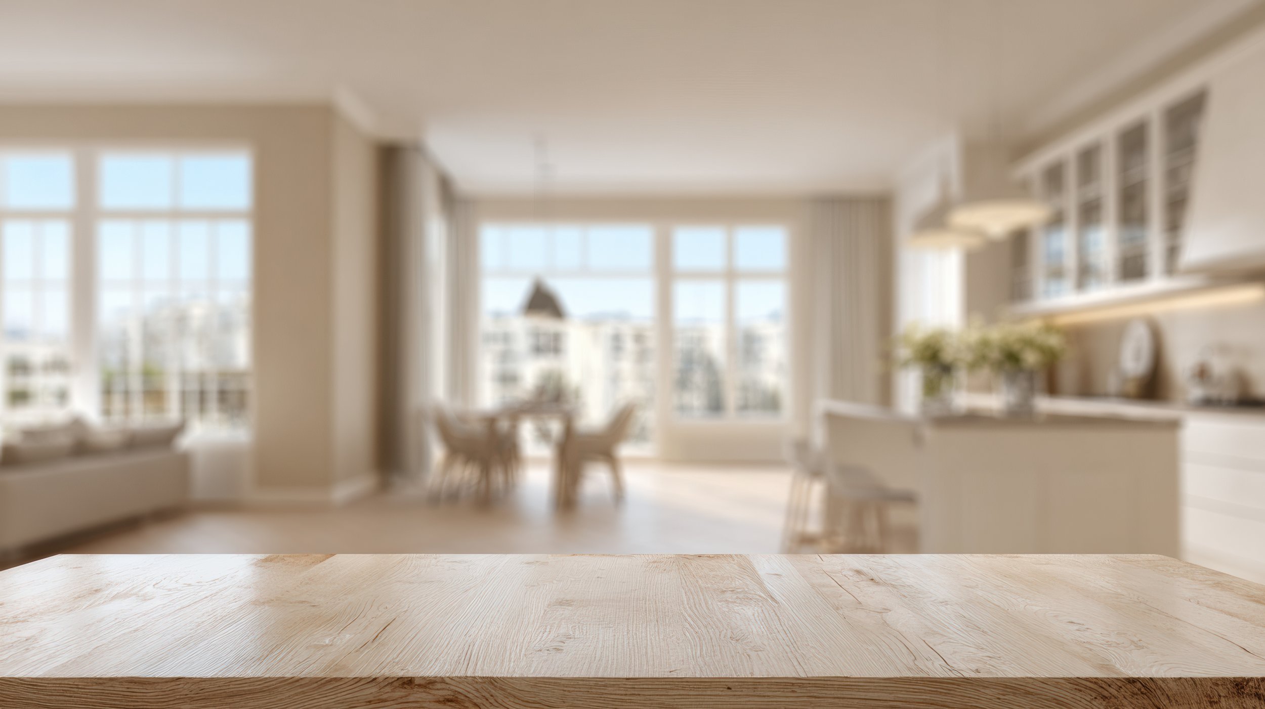 Blurred image of a bright, modern kitchen and dining area with large windows, a table, and chairs.