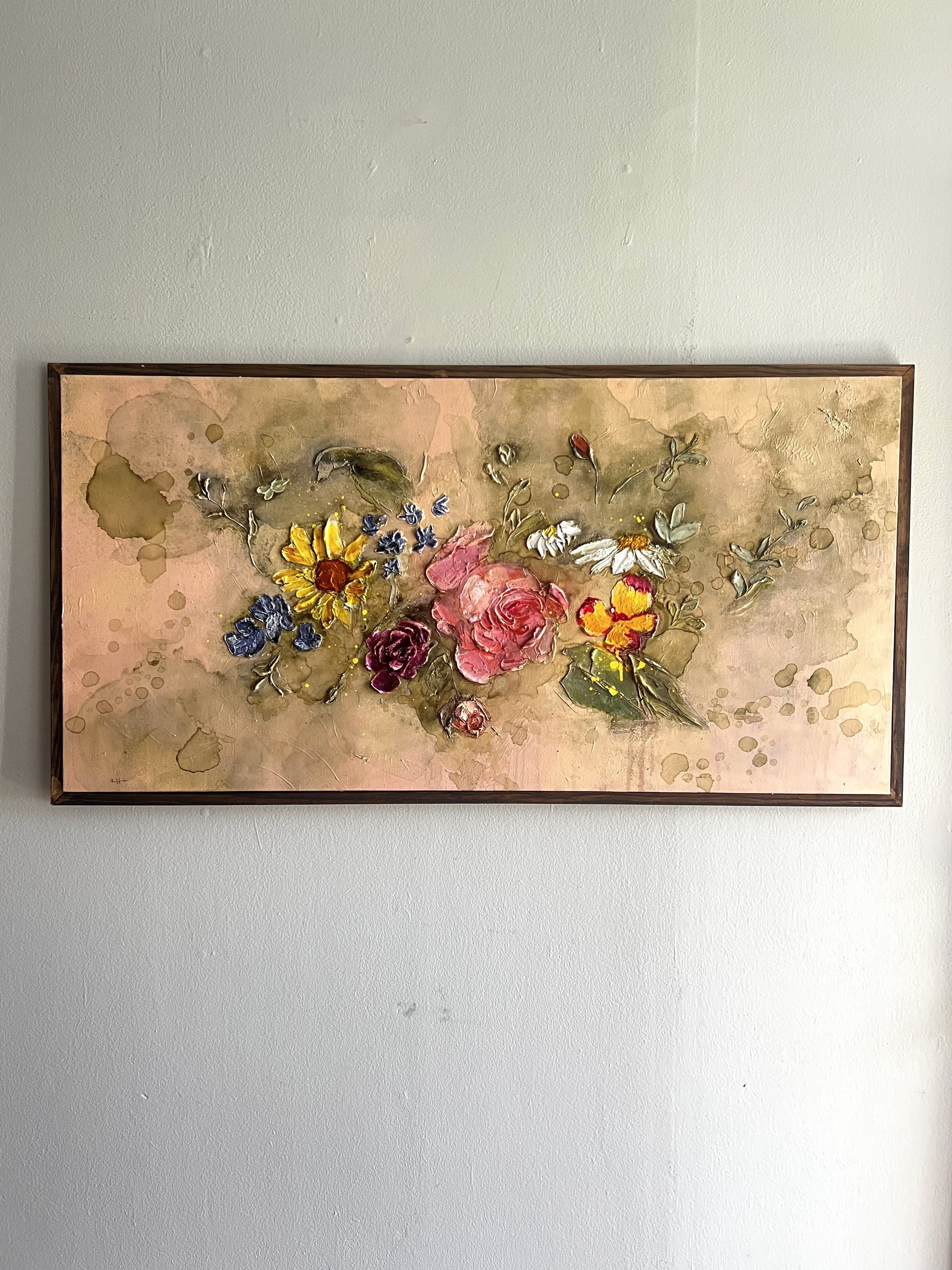 Framed watercolor painting of a mixed bouquet of colorful flowers, including daisies, roses, and pansies, hung on a plain white wall.