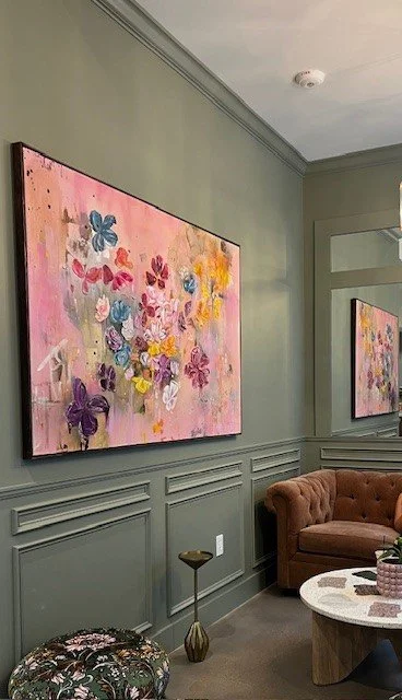 Living room with green wall paneling, a framed artwork of colorful butterflies, a pink tufted sofa, a round marble coffee table, and decorative items.