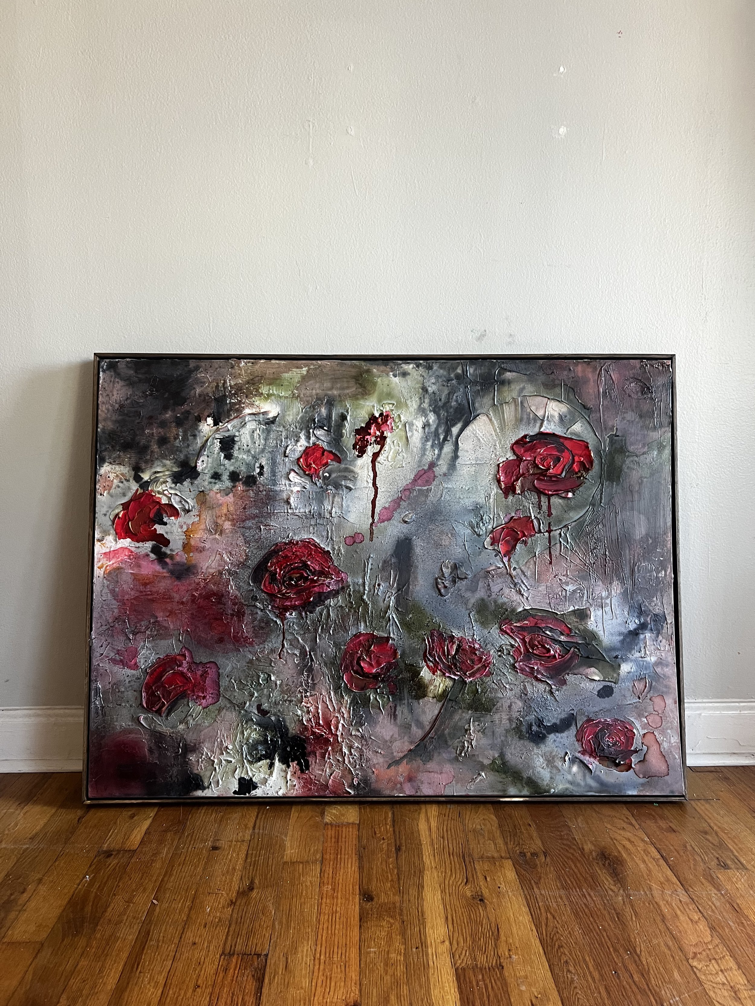 Abstract floral painting with red roses on a textured gray and black background, leaning against a plain light-colored wall and resting on a wooden floor.