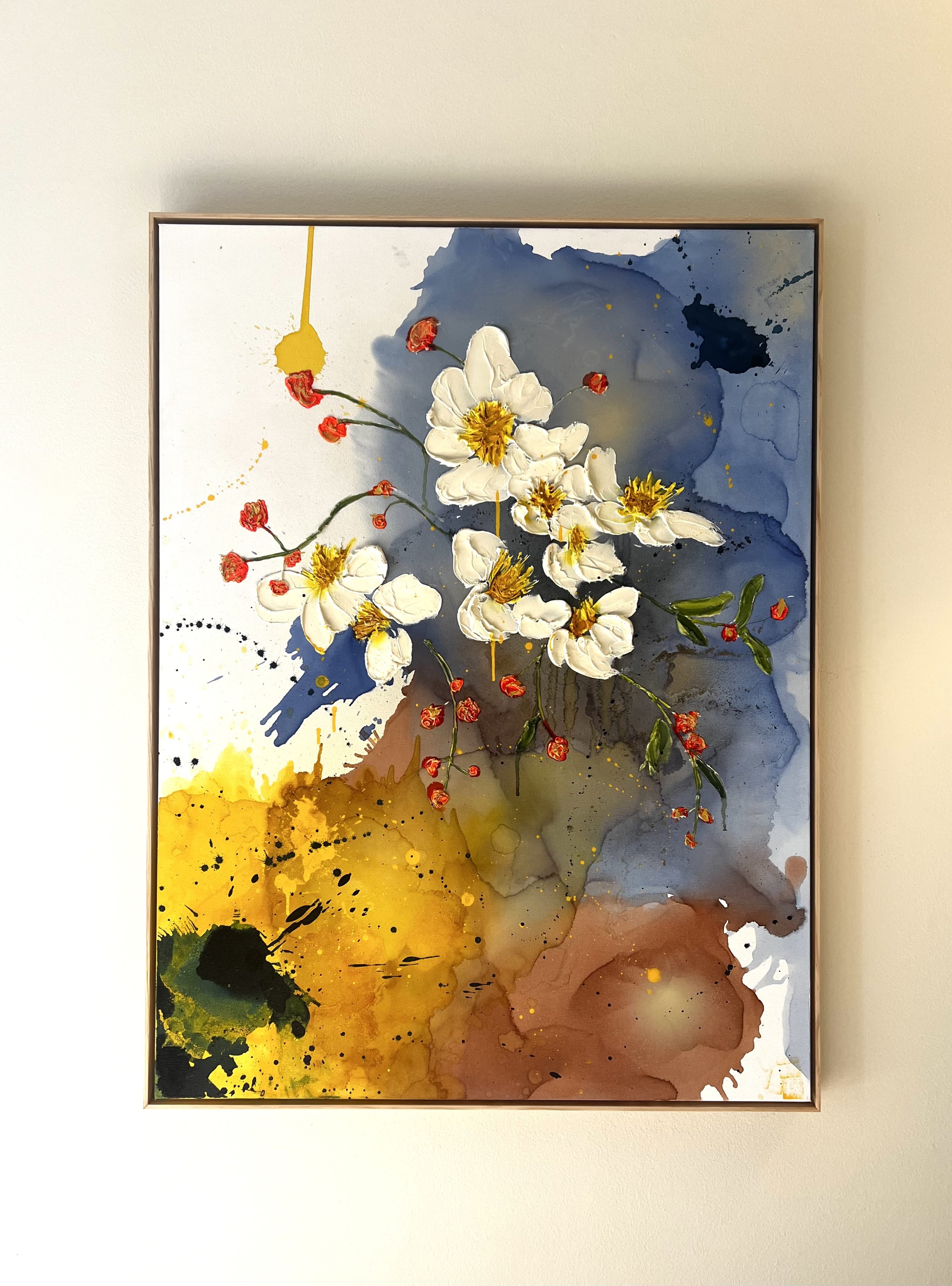 A framed abstract painting with white flowers and red accents set against a background of blue, yellow, and brown watercolor splashes.