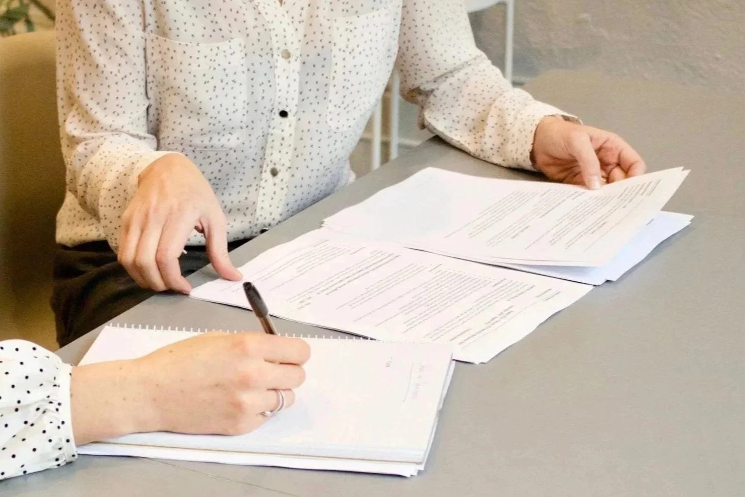 Two people reviewing and signing documents at a table, with one person writing on a stack of papers.