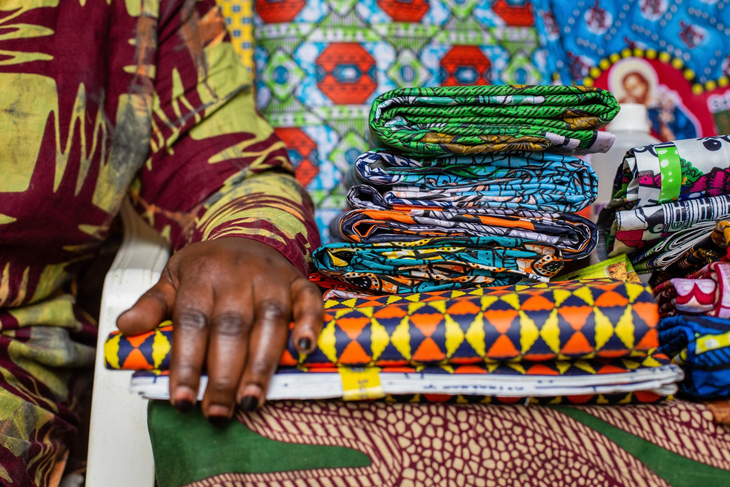 Furaha rests her hand on a pile of African wax print fabrics folded and piled up.