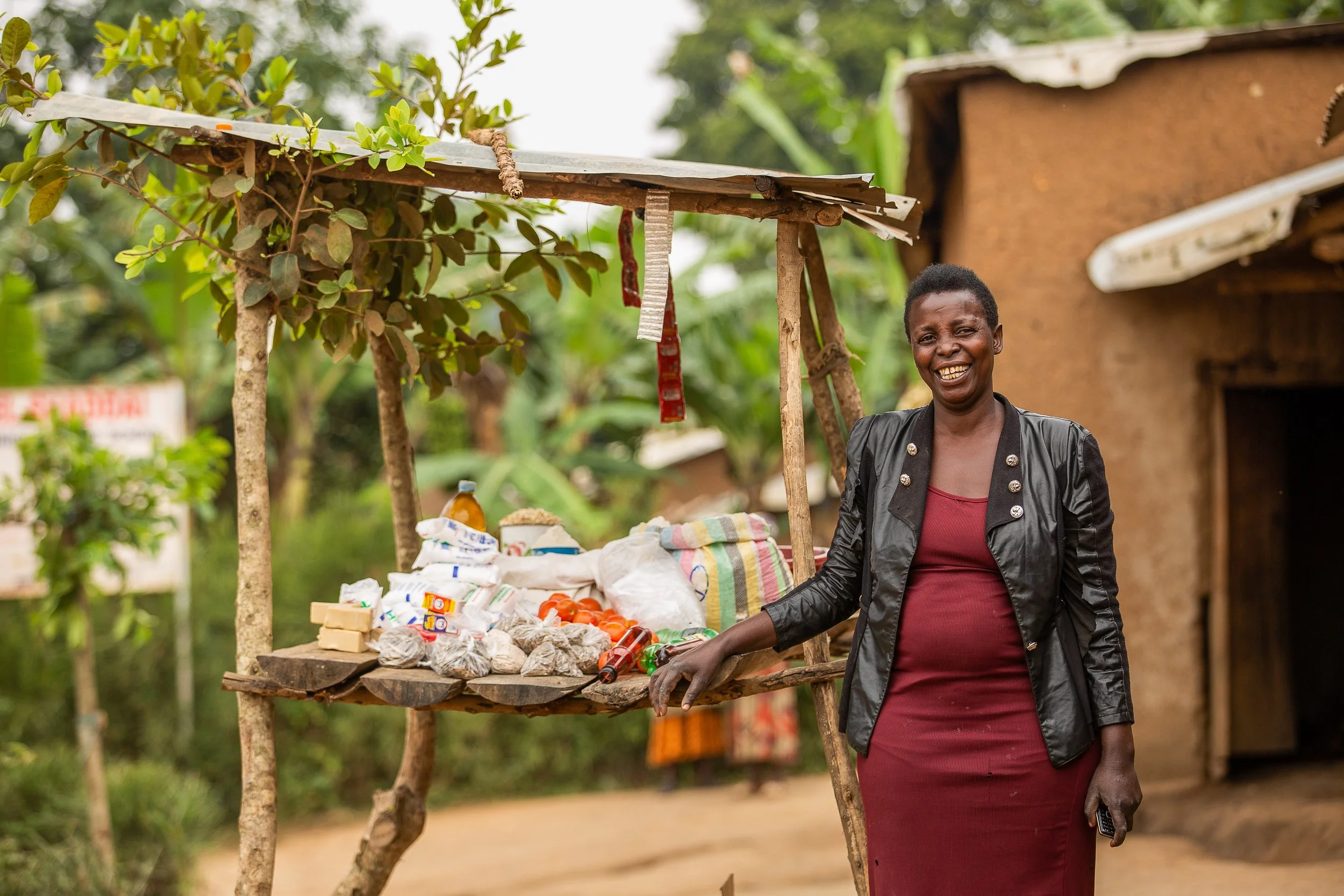 Salama stands next to her groceries stall - a simple wooden structure with produce on a table top.