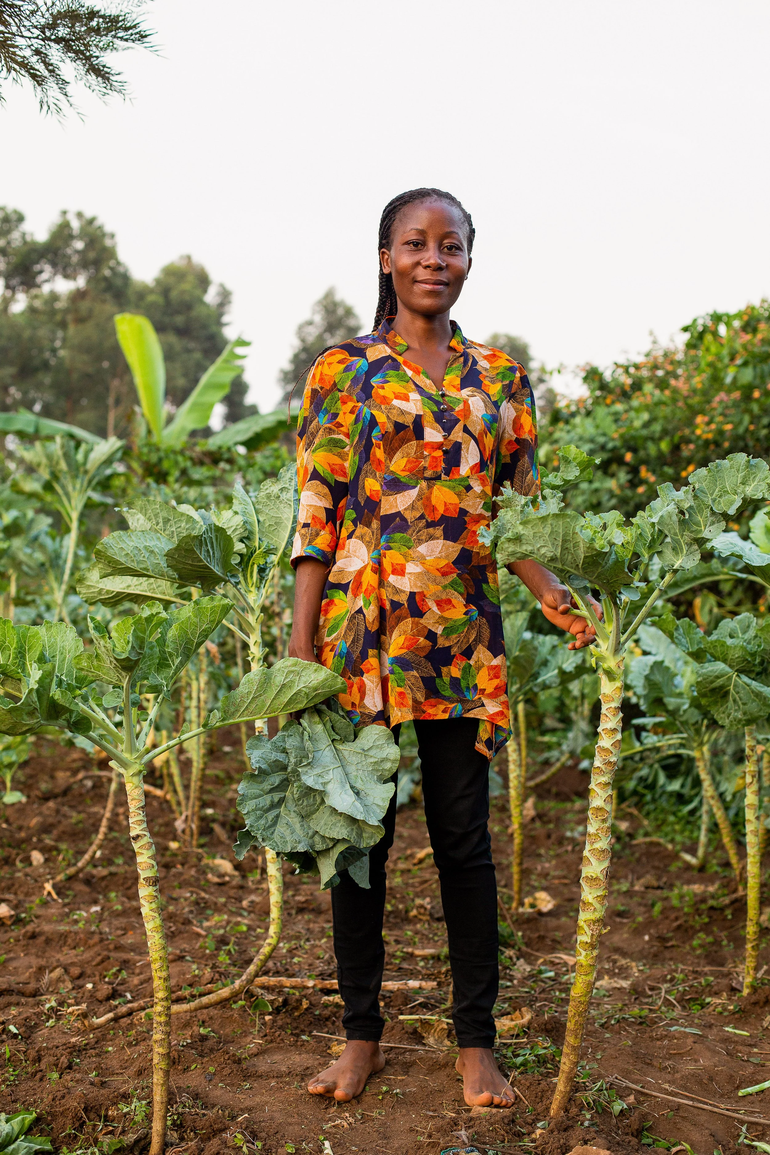 Ruth stands in her kale field at sunset, her hand resting on top of a farm tool.