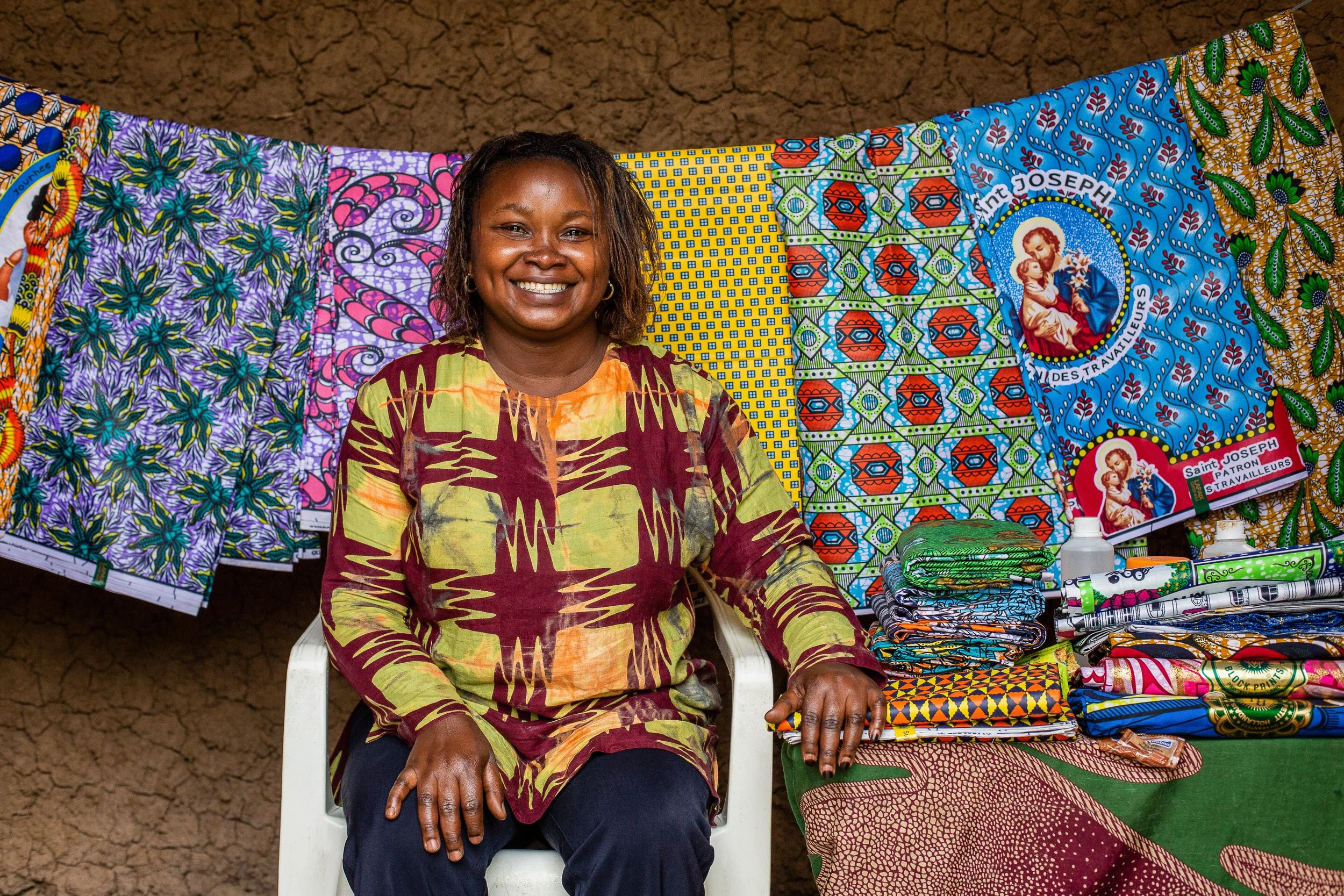 Furaha sits in front of African wax print fabric hanging up. 