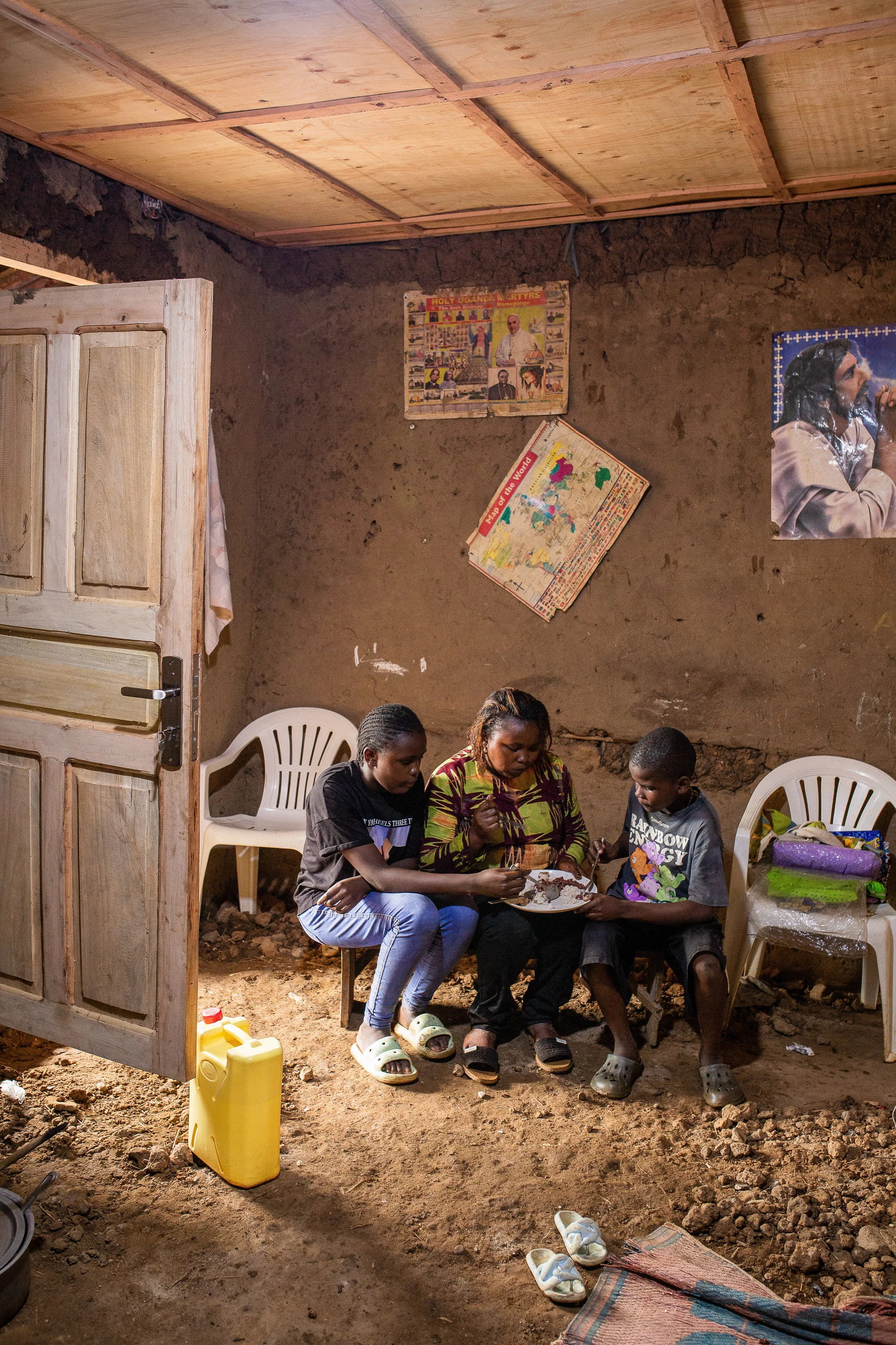Furaha and her children sit in their home sharing a meal from one plate. 
