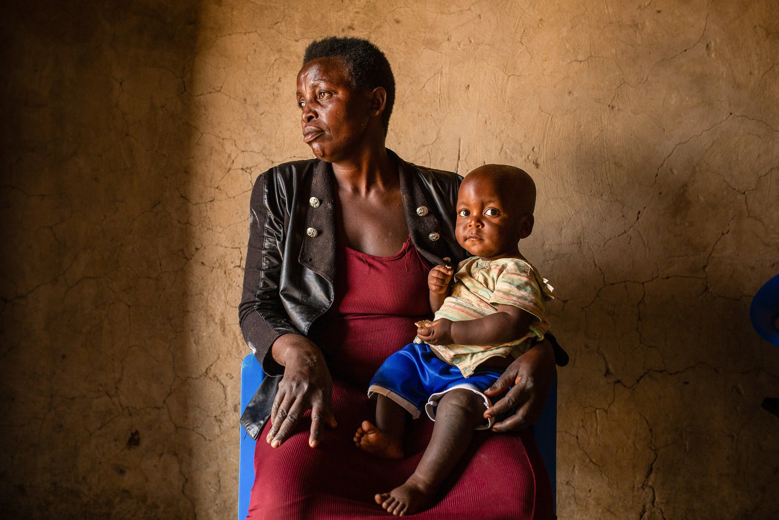 Salama sits inside her home holding her youngest child, who looks curiously at the camera. 