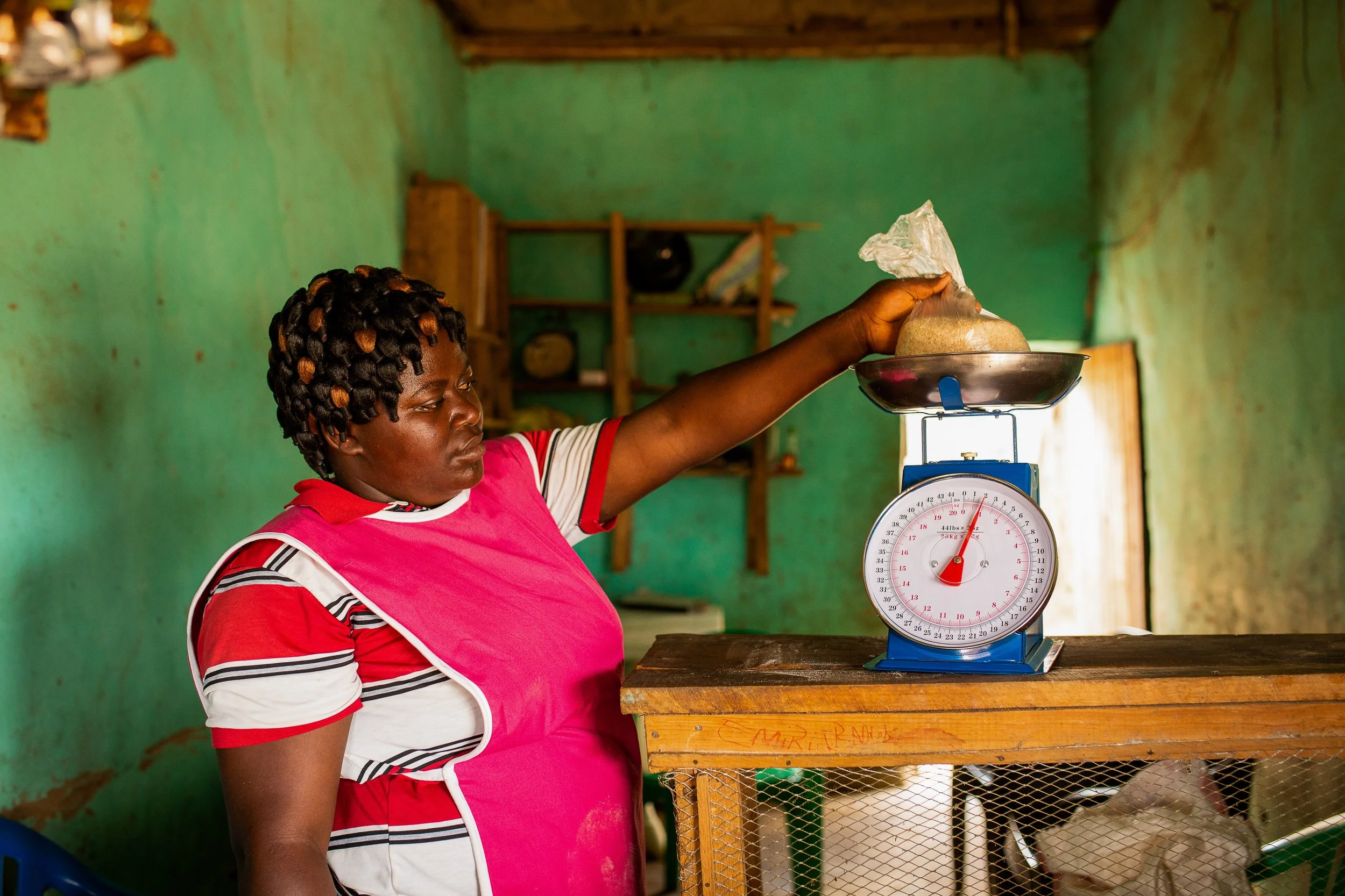 Mediatrice weighs rice in a bag in her grocery shop