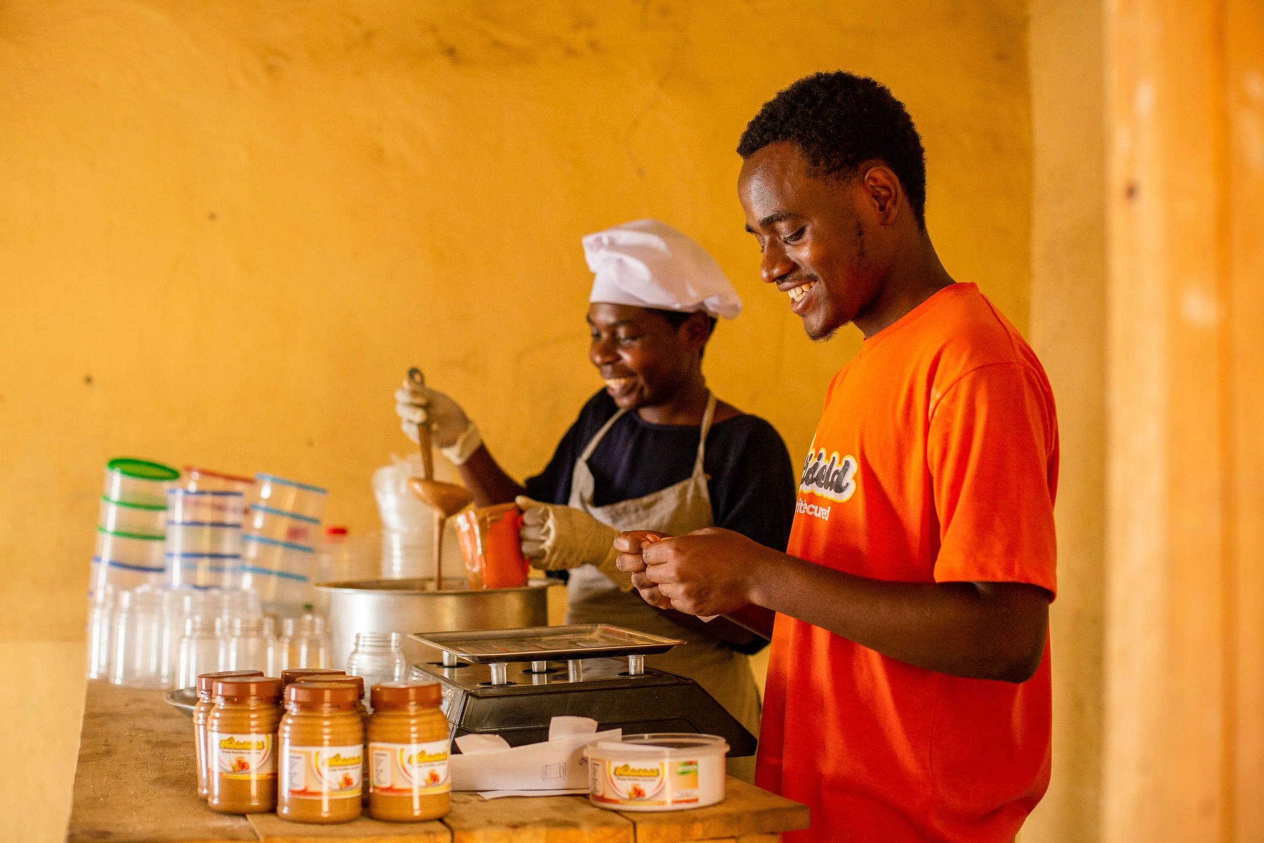 Savino and an employee smile as they jar up peanut butter and add labels to them.