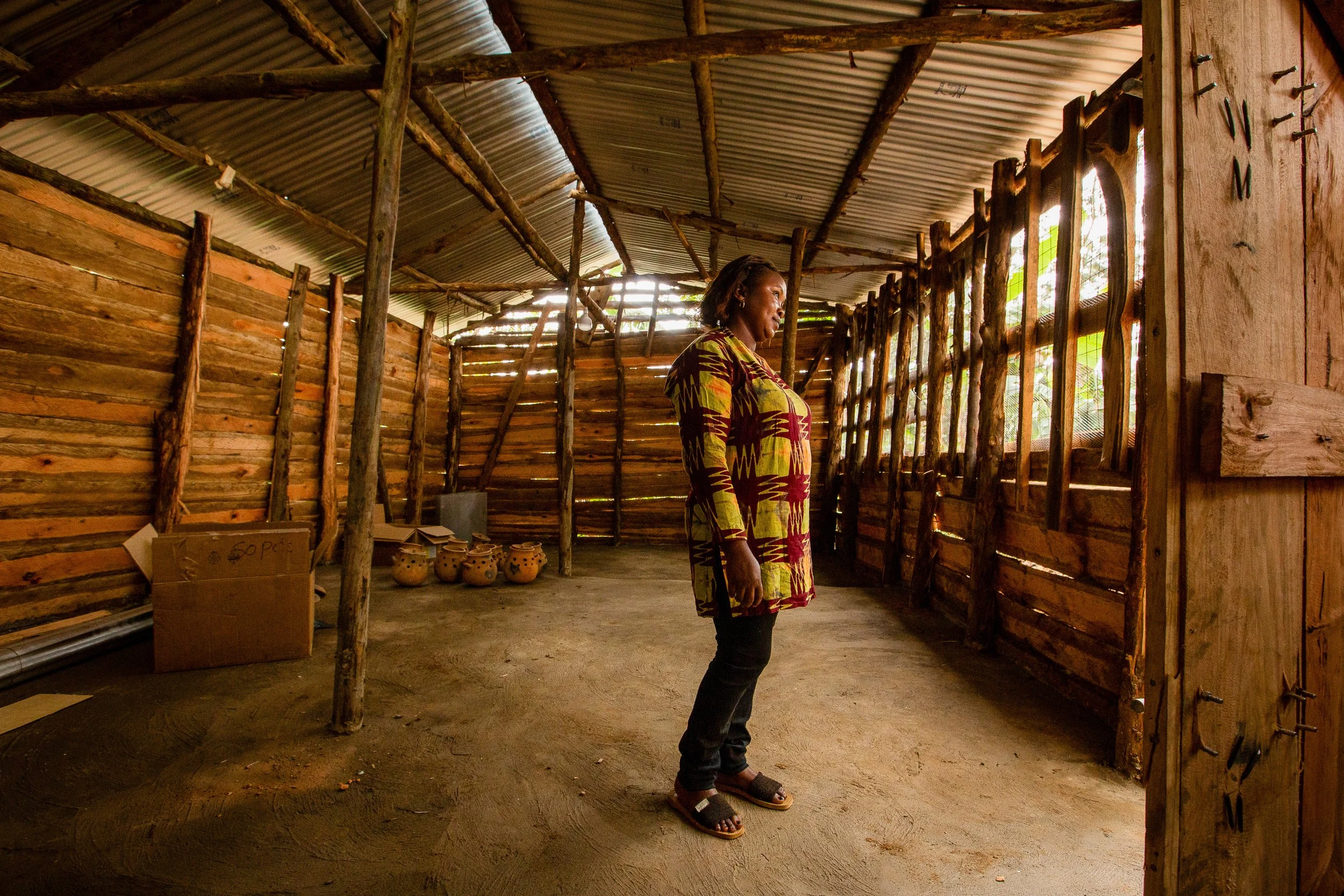 Furaha stands in a wooden warehouse, facing the door and look outwards