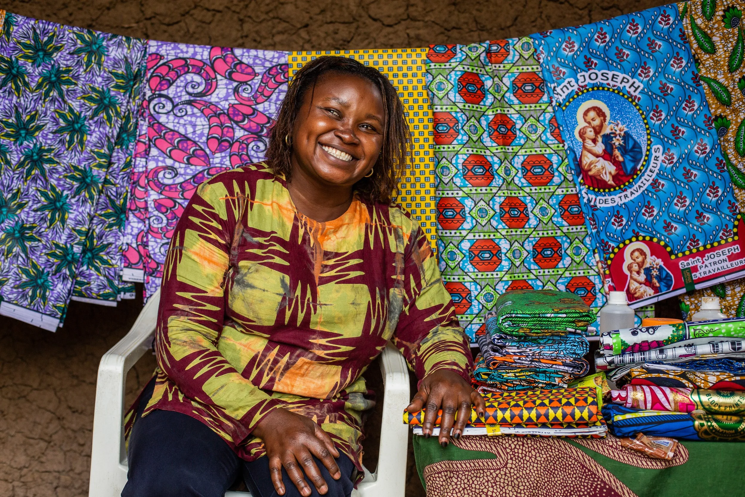 Furaha sits in front of African wax print fabric hanging up. 