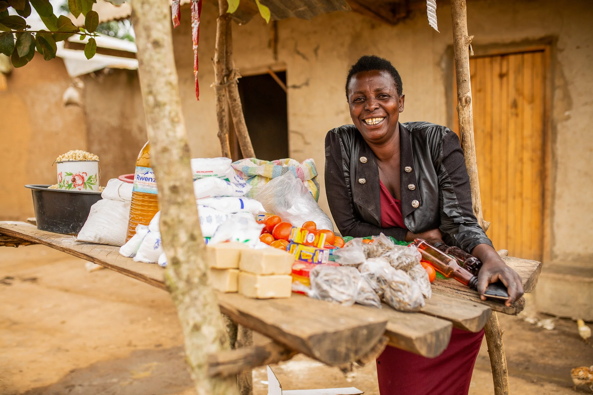 Salama shares a big smile and leans against her groceries stall outside her house. 