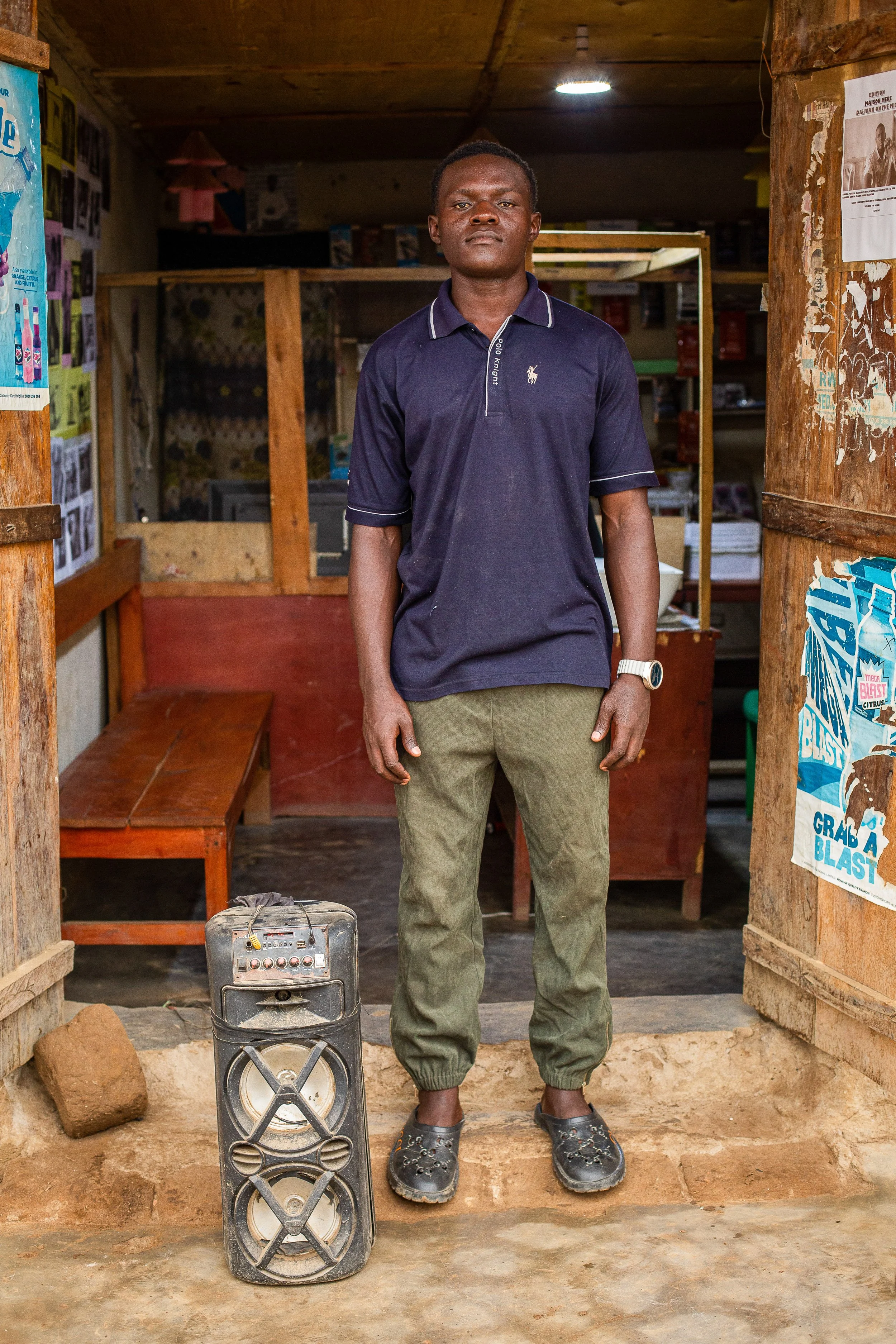 Alfred stands in his shop next to a speaker on the ground. 
