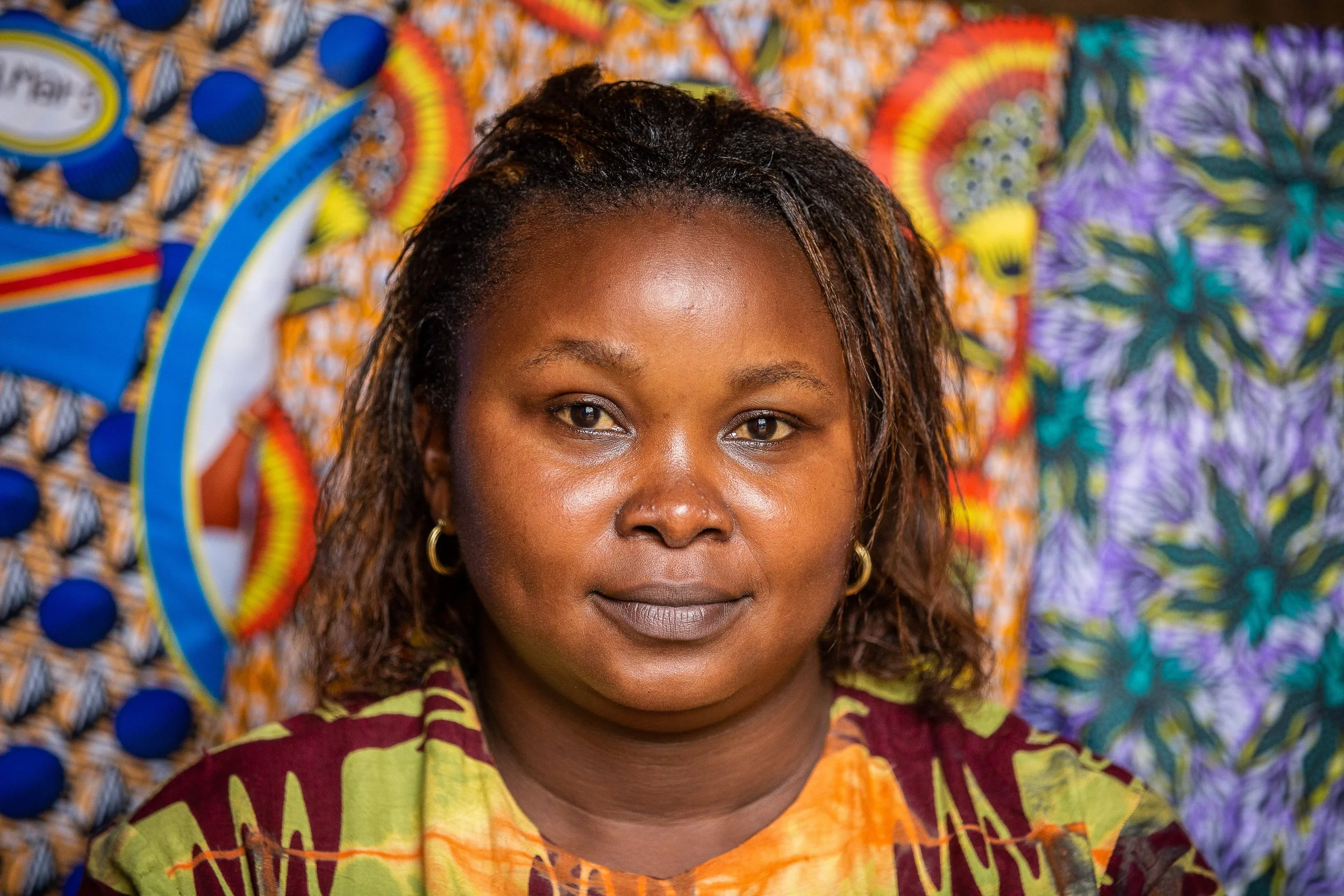 Furaha looks into the camera. Behind her is an African wax print fabric.