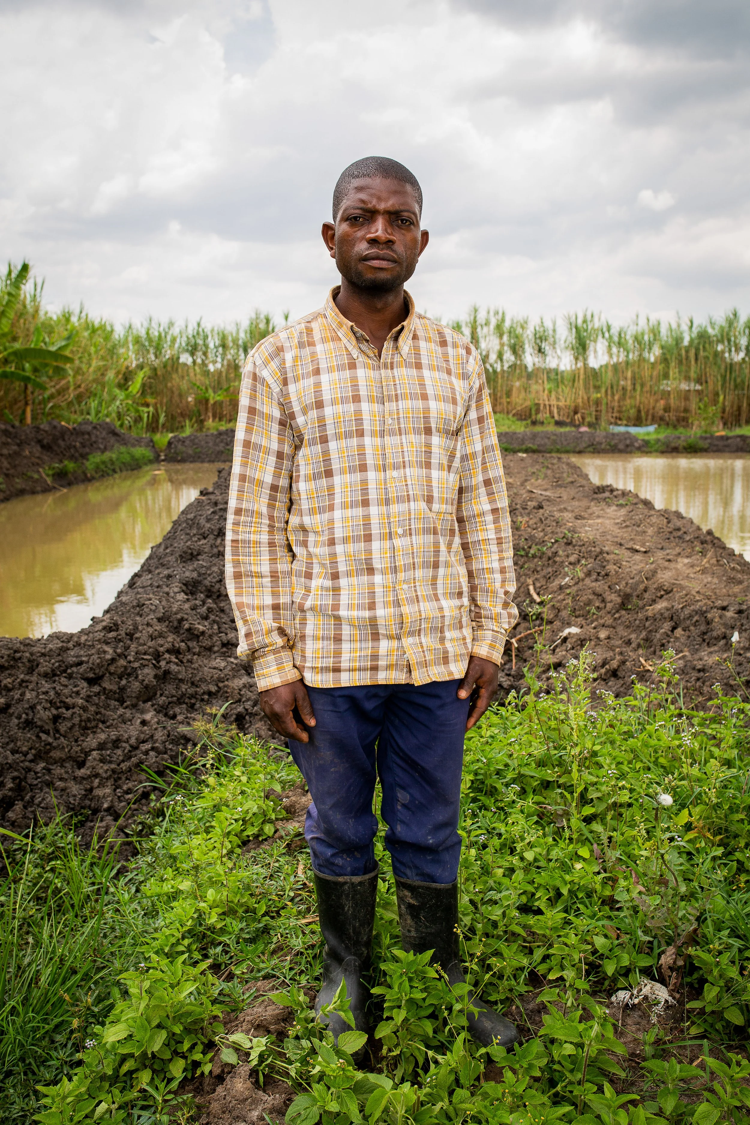 Joshua stands in his fish farm wearing a chequered shirt. 