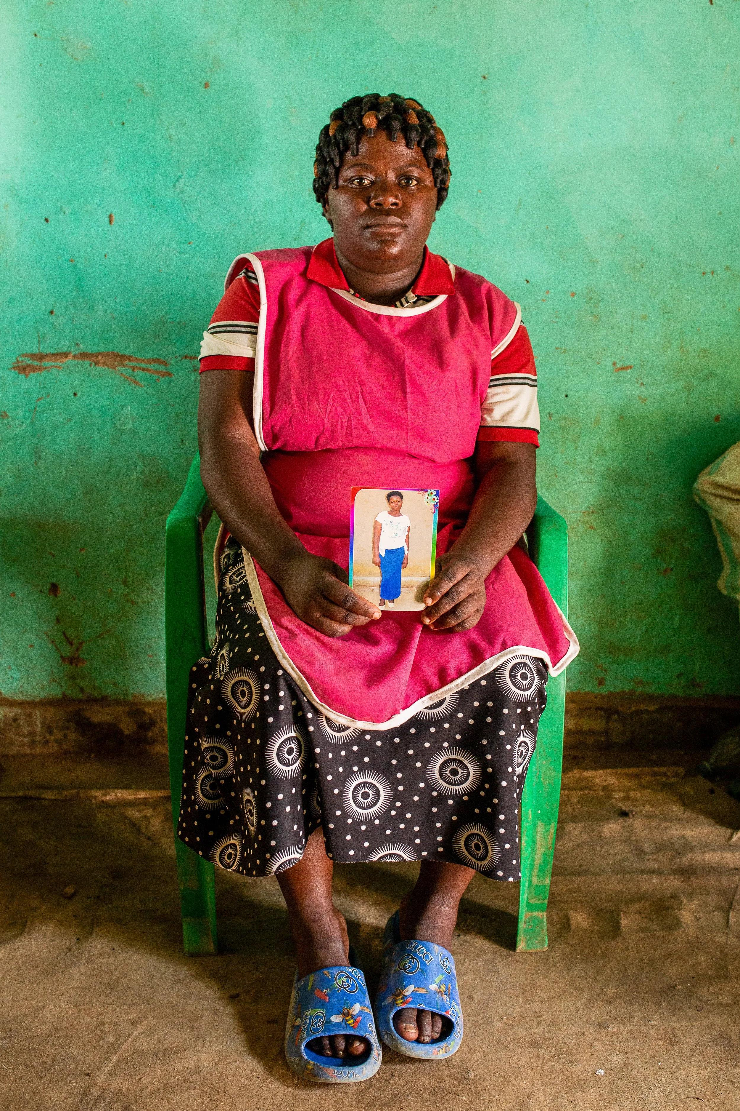 Mediatrice sits holding a photograph of her sister in her lap.
