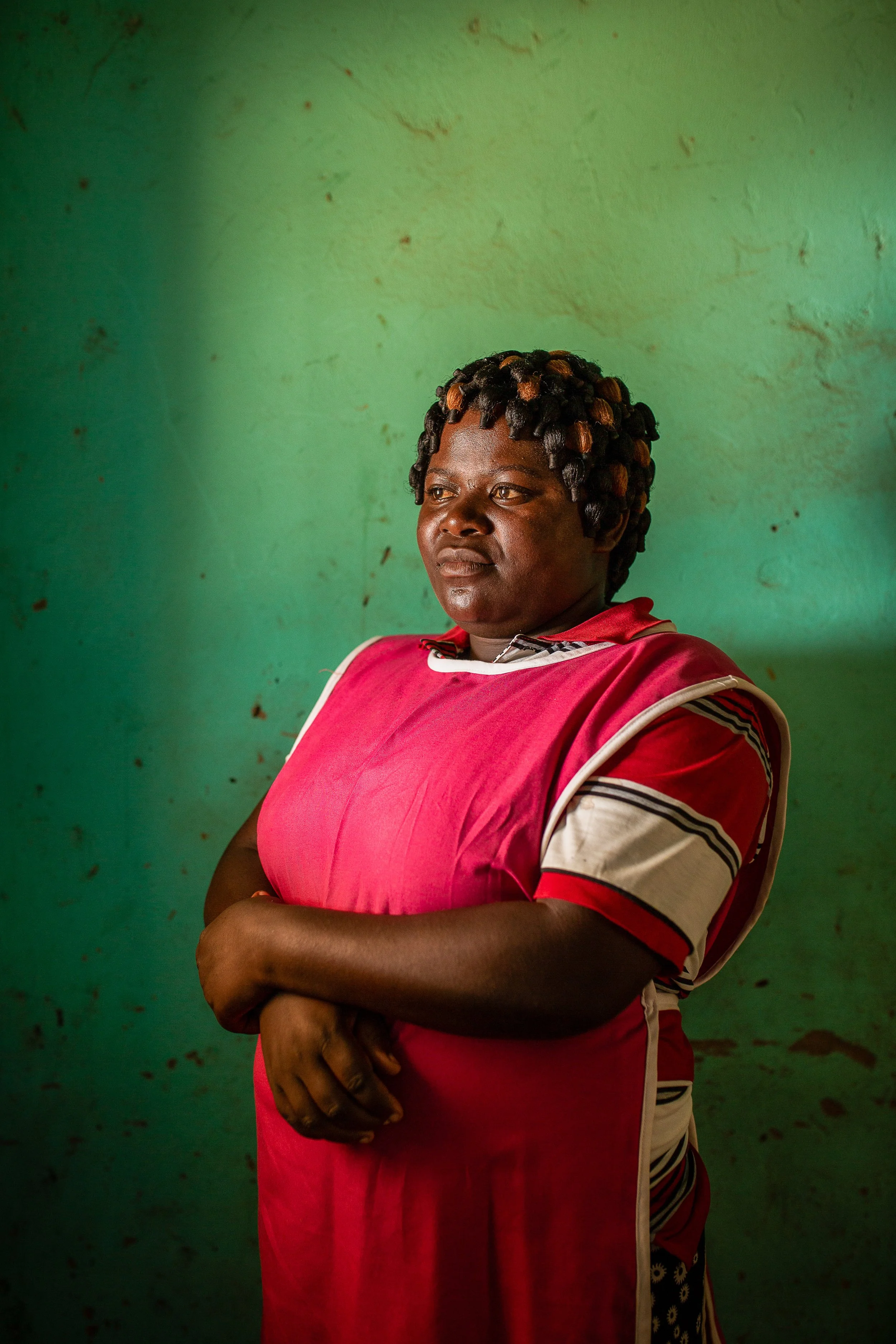 Mediatrice looks off to the right of a camera, she is wearing a pink apron and against a green painted wall.