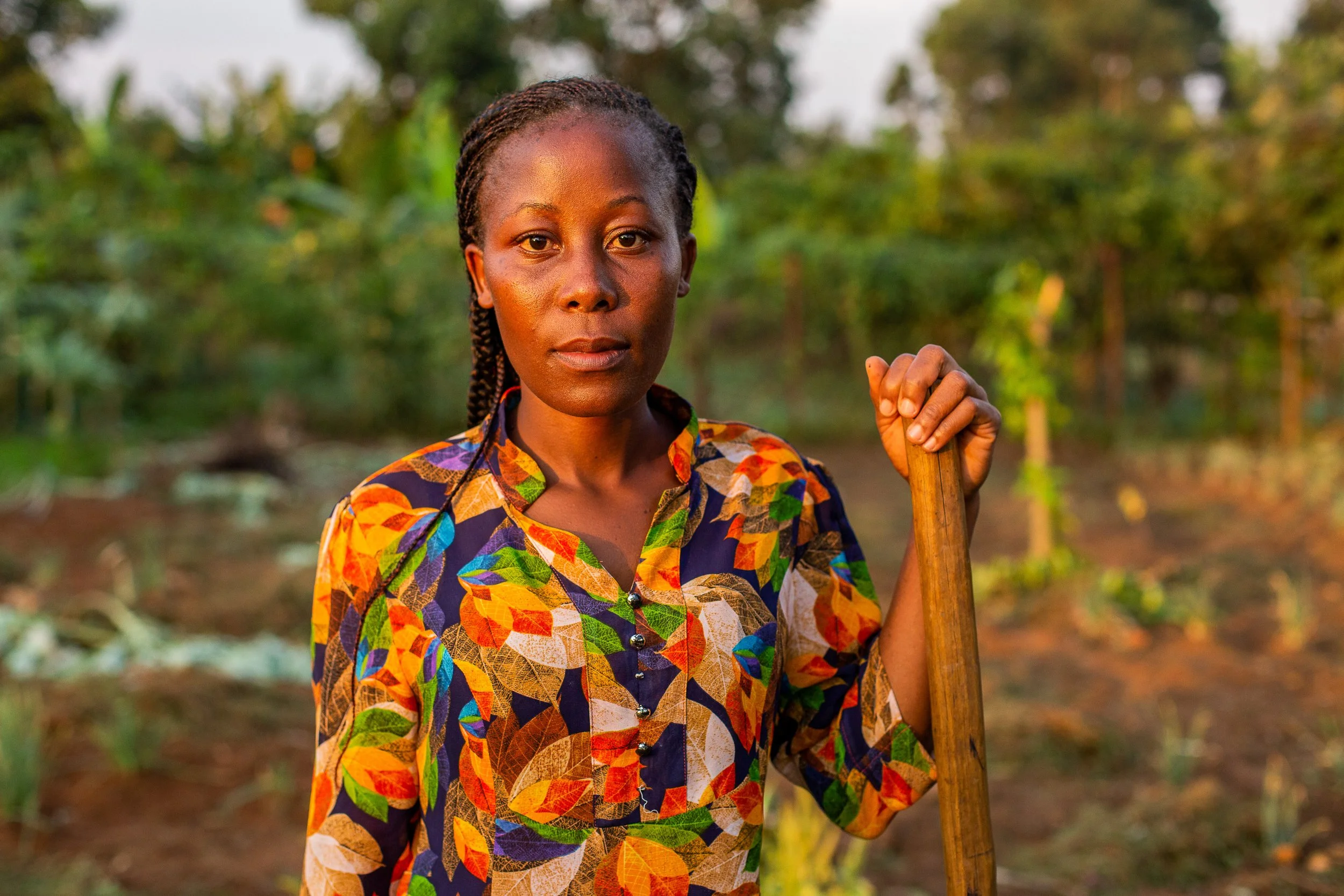 Ruth stands in her kale field at sunset, her hand resting on top of a farm tool. 