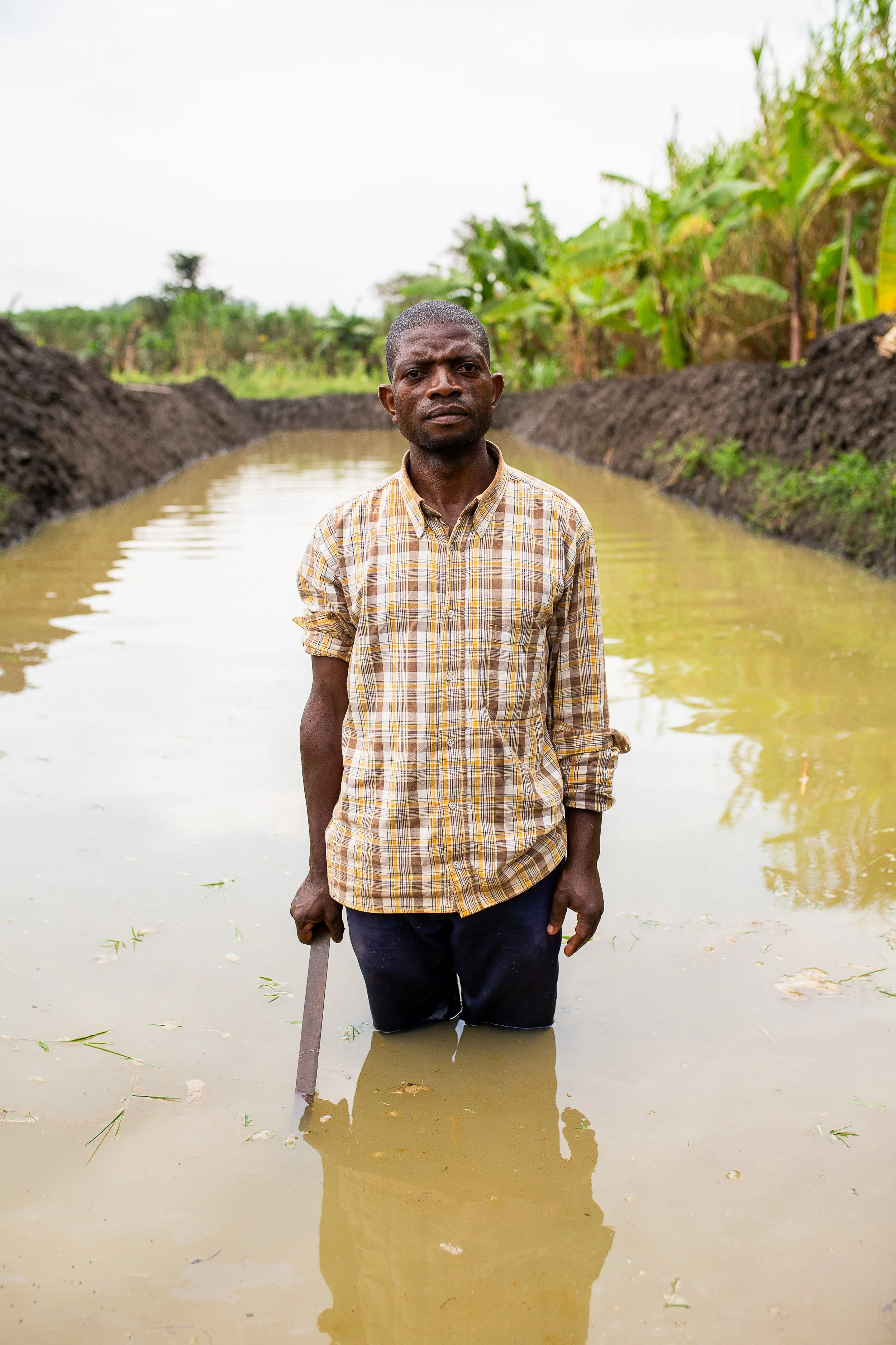 Joshua stands in his fish farm, knee deep in water. 
