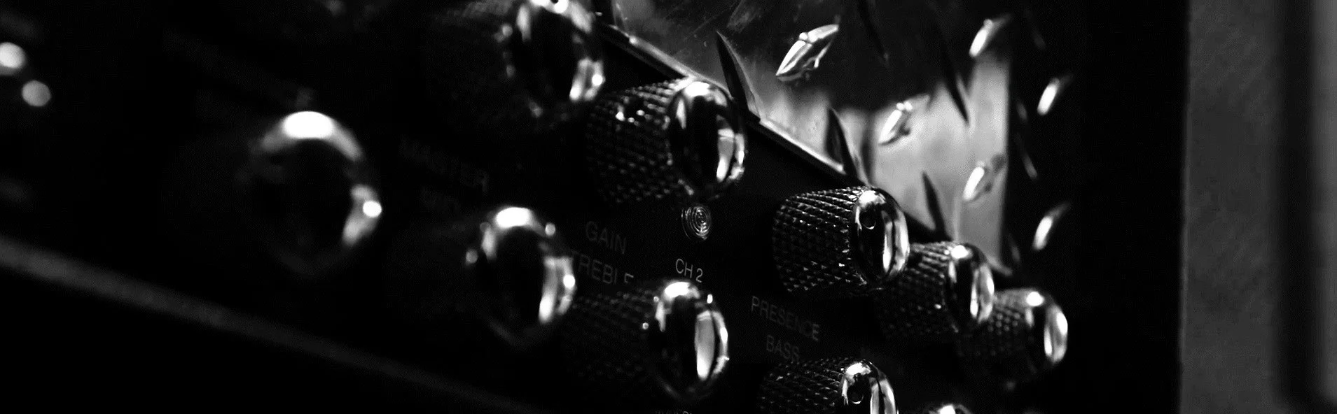 Close-up of guitar amplifier controls with black and silver knobs, labeled gain, treble, channel 2, presence, and bass, in black and white.