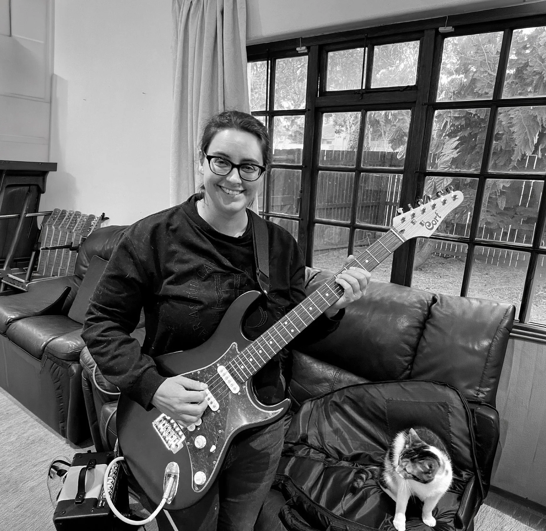A woman shopping with her dog, holding a guitar inside a home with large windows and a backyard, black and white photo.