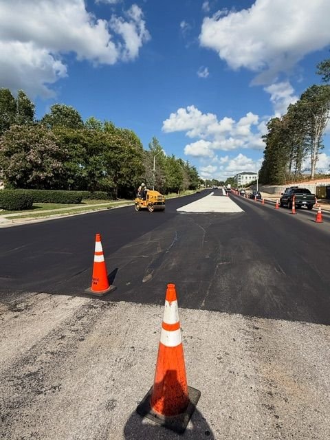 road in the process of being paved with construction equipment, flanked by orange traffic cones