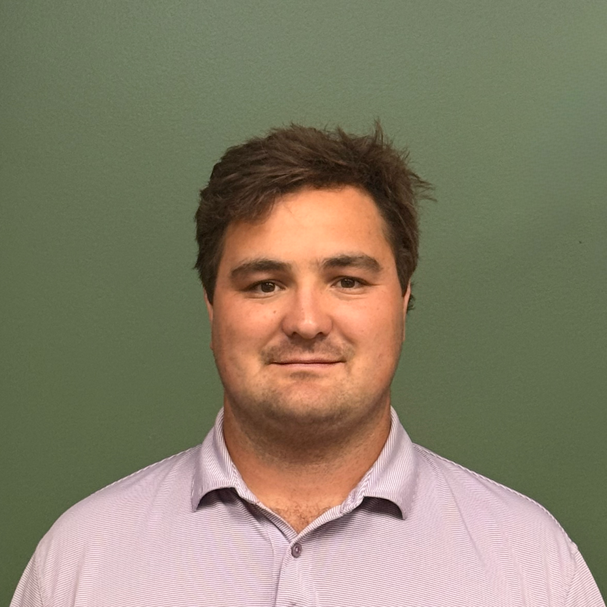 Close-up of C&B Construction Partners President Peyton Crone, wearing a purple and white striped dress shirt and a dark tie, against a green background.