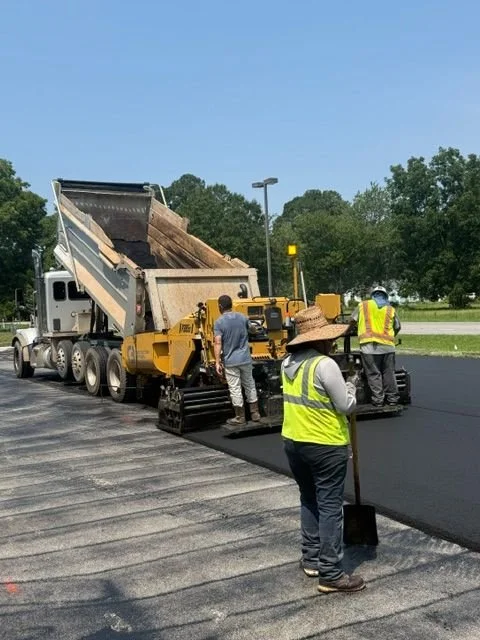 white truck pouring asphalt onto road surrounded by workers