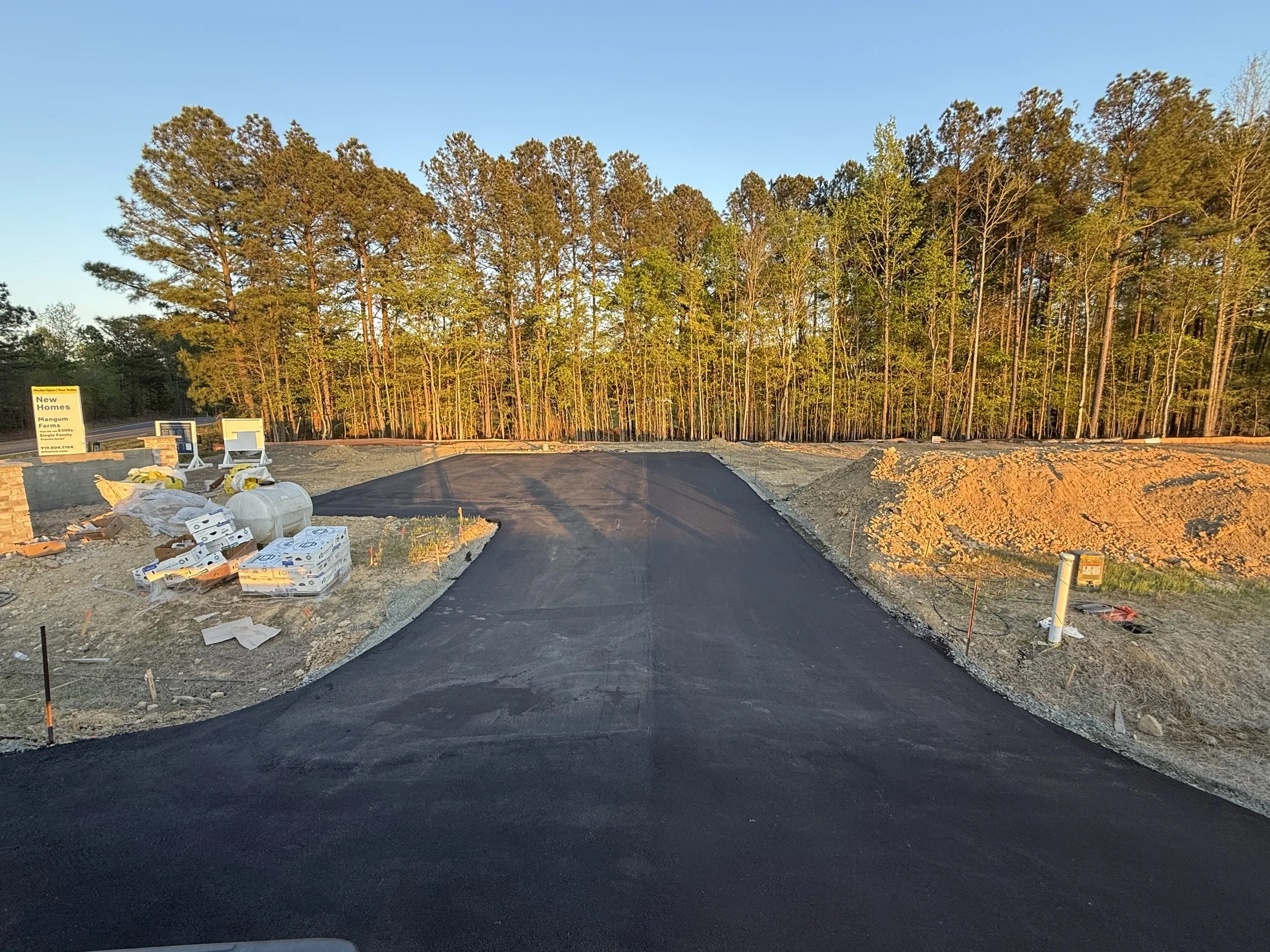 asphalt pavement surrounded by dirt with a row of green trees in the background