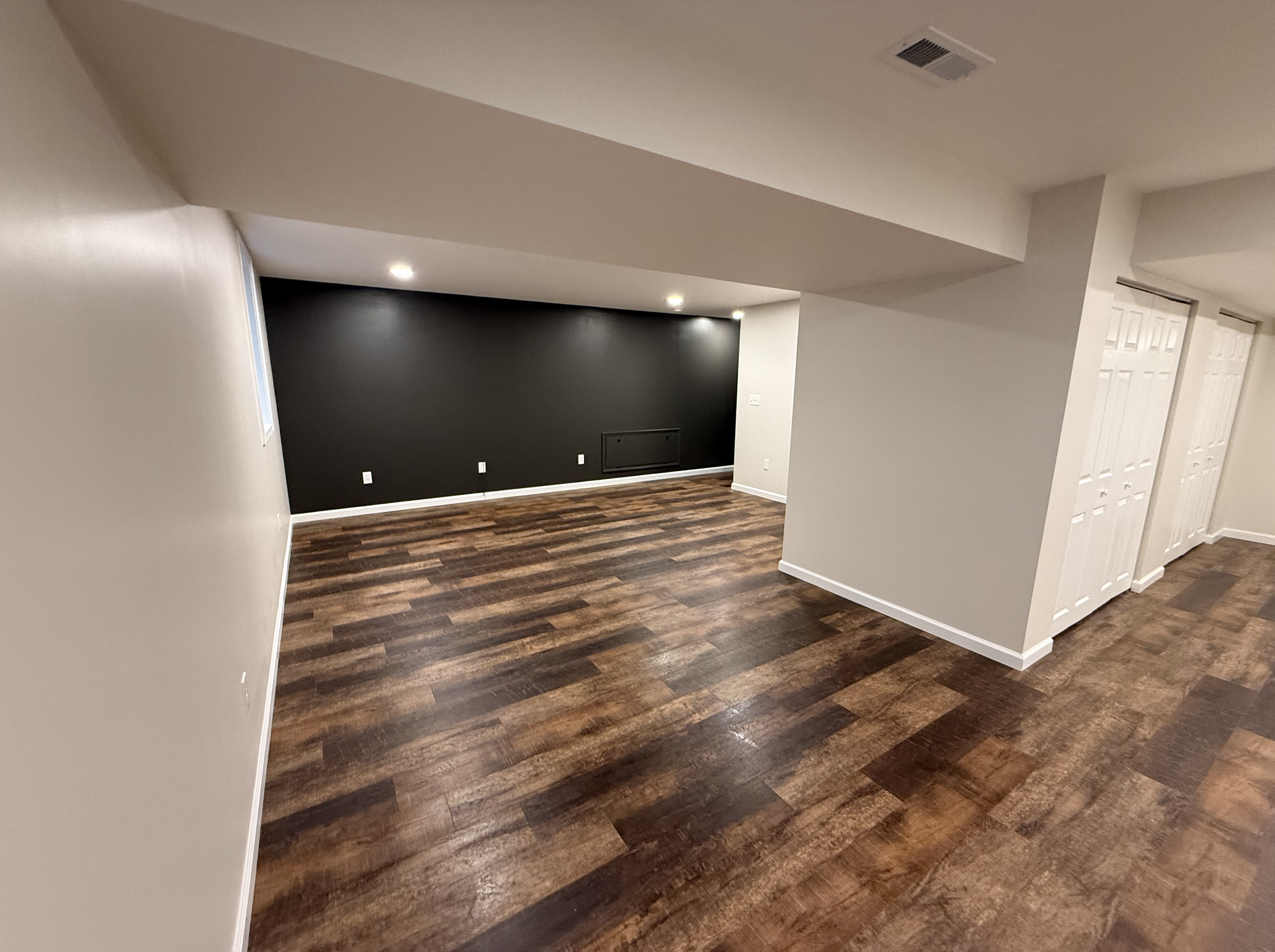 Empty room with dark wood flooring, white walls, a black accent wall, recessed lighting, and a vent on the ceiling.