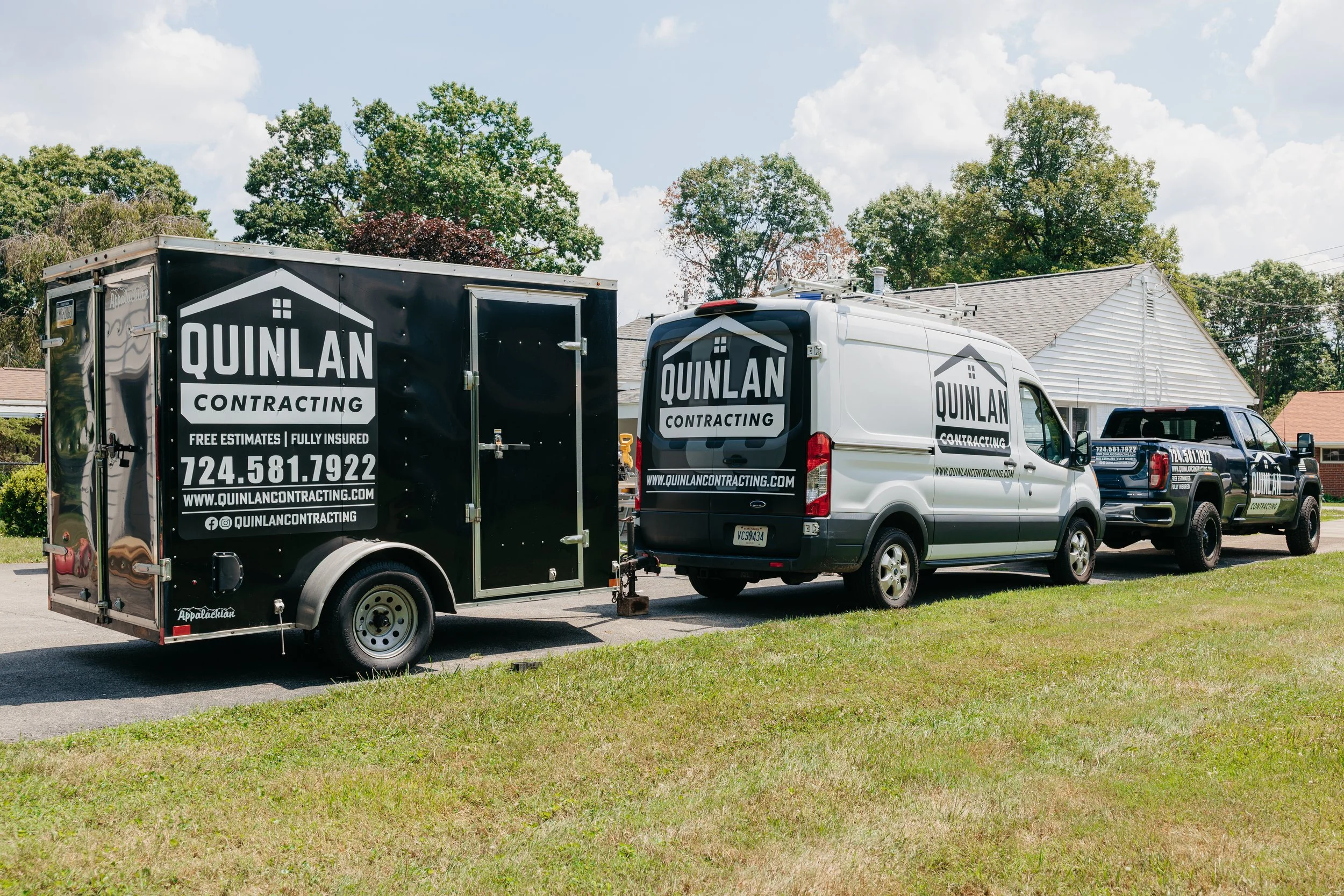 White van with black logo and trailer for Quinlan Contracting, parked on a suburban street with trees and houses in the background.